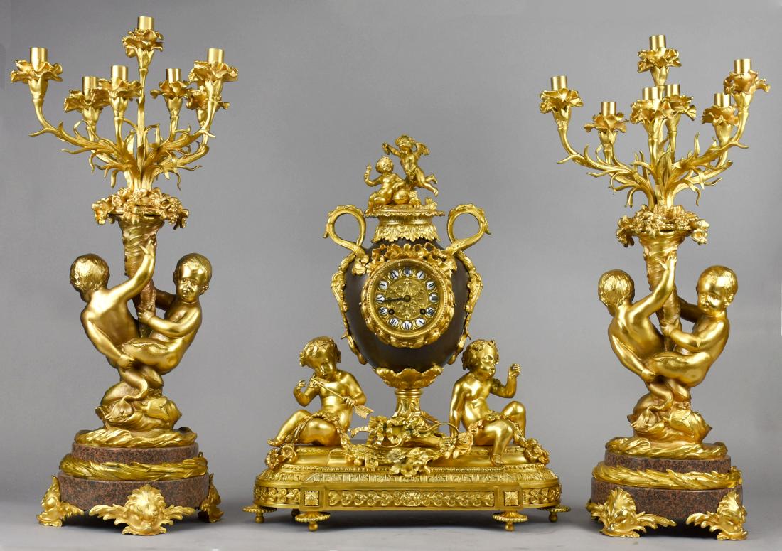 Antique Neoclassical French Ormolu Clock Garniture: Absolutely stunning antique neoclassical clock garniture. Clock features two putti, one holding a torch atop an urn shaped clock case, encased in ormolu acanthus leaf and ribbon details. The hand pain