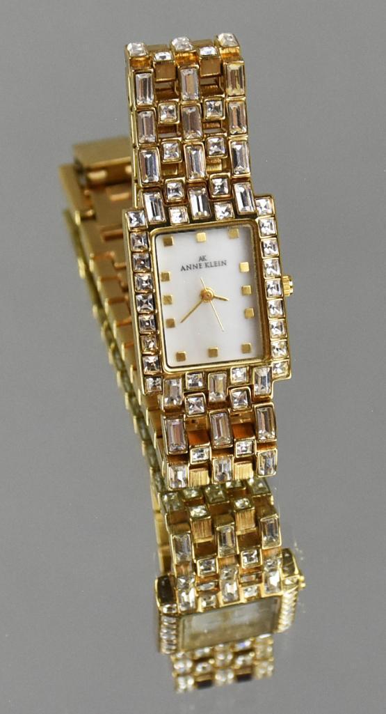Anne Klein Gold Crystal Band MOP Ladies Watch: Beautiful ladies gold toned and crystal tank style watch by Anne Klein. The chain style band is encrusted with clear crystals set in a gold tone band with a Mother of Pearl dial face. Band closure is