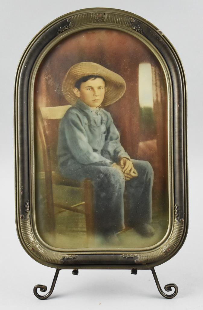 c1920 Colorized Photo Young Farm Boy: Darling colorized photo of a young boy in his farmer garb. Unknown maker and framed in a pre Art Deco frame painted black with applied details. Original framing by the Fine Arts Association, remnants