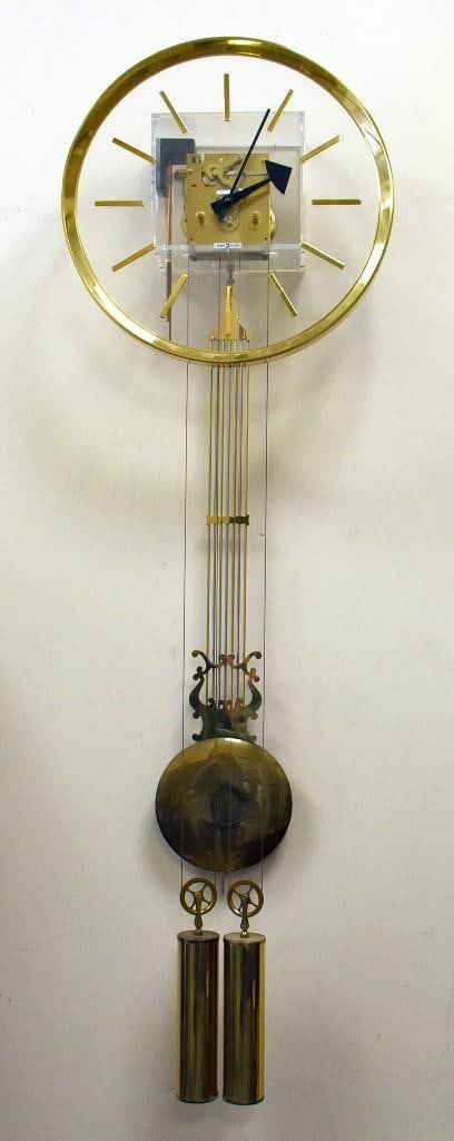 c1970 Arthur Umanoff for Howard Miller Lucite/Brass Clock: Very cool Howard Miller clock designed by Arthur Umanoff from the 1970s. Wall clock with movement cased in lucite, cable driven. Clear dial with brass numerals and brass pendulum and weights. Model nu