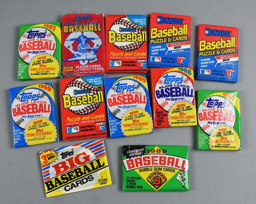 1980s Baseball Card Wax Packs by Topps Donruss Fleer Bowman: 11 unopened wax packs of baseball cards from the 1980s. Includes packs from Topps, Donruss, Bowman, and Fleer, each featuring classic branding and some containing puzzle pieces or gum. These vintage p