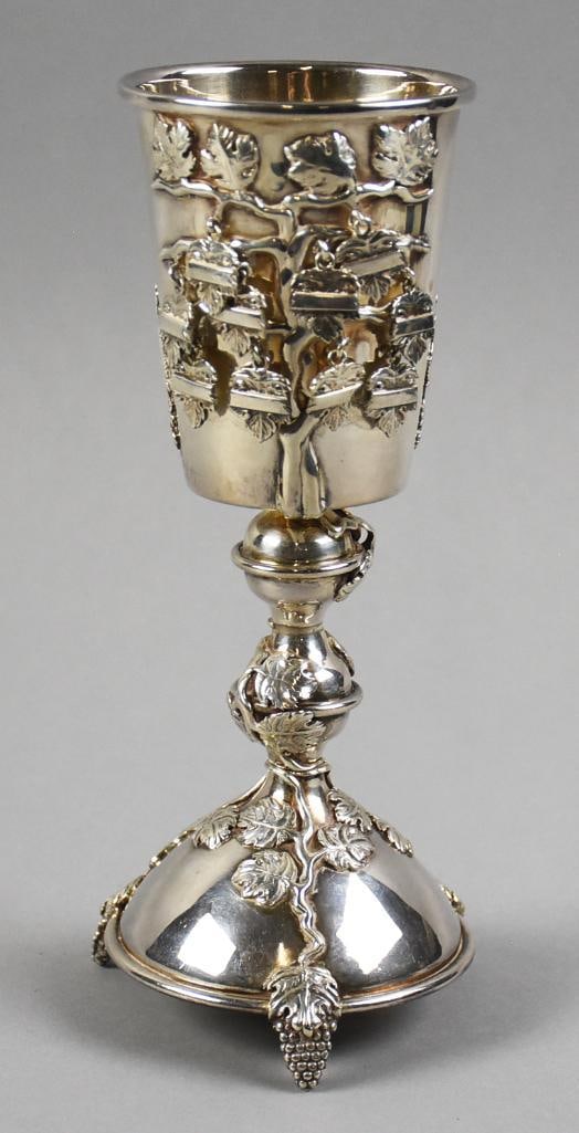 Michael Ende Sterling Kiddush Cup: The cup has grape leaves throughout the body with lions flanking a quote in Hebrew on one side. The vines carry down the stem with the feet being grape bunches. The quote (translated online):