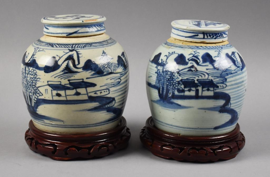 Antique Chinese Canton Blue & White Lidded Jars on Stands: This is a stunning pair of Chinese porcelain jars. Each Canton piece is blue and white, hand decorated and on stands that appear rosewood. Each scene is a landscape with a gentleman fisherman. Each