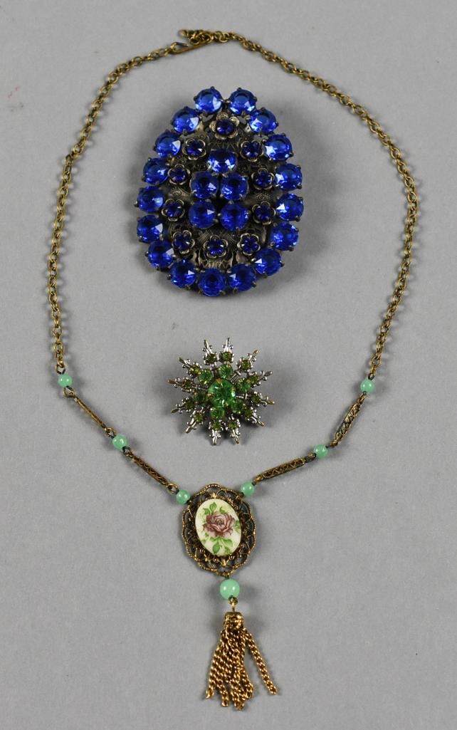 Vintage Costume Necklace and Brooches: Beautiful costume jewelry pieces that includes a gold tone necklace with porcelain flower pendant and fringe and two rhinestone brooches, one with peridot green and one with cobalt. No visible marks.