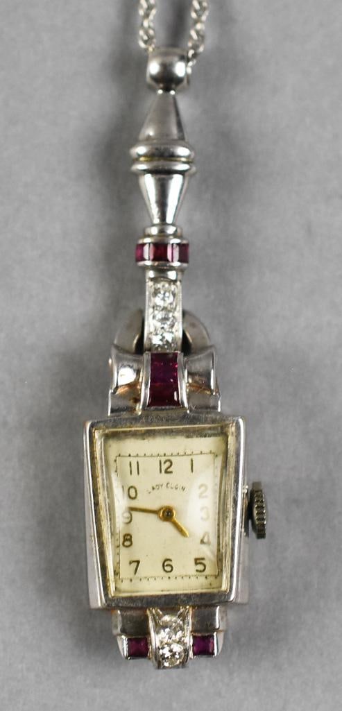 14k Lady Elgin Diamond Ruby Pendant Watch: Vintage Lady Elgin mechanical pendant watch crafted in 14K white gold and accented with diamonds and red gemstones appearing to be rubies. The rectangular dial is signed “Lady Elgin” and featu