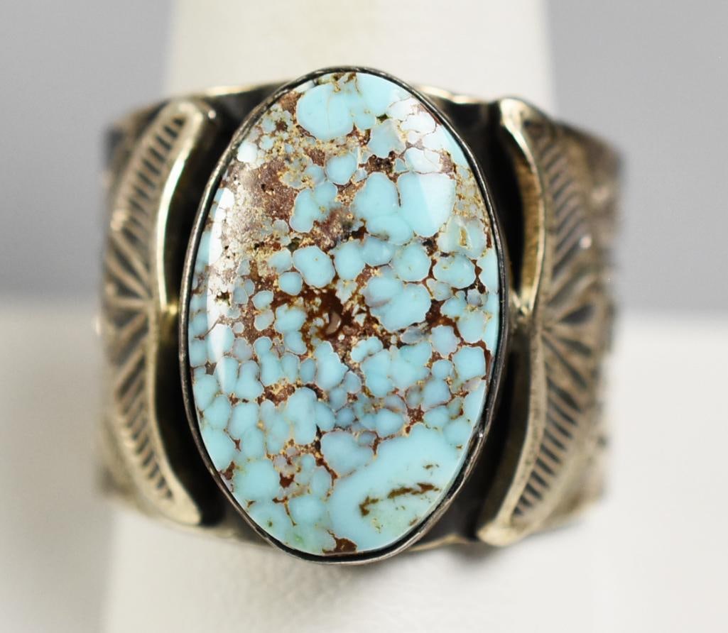 Vintage June Delgarito Navajo Sterling Turquoise Ring: Wonderful ring from Navajo jewelry artist, June Delgarito. It is sterling silver with clouds and waves symbols, a center polished turquoise stone that is flanked by applied wings. Signed inside the ba
