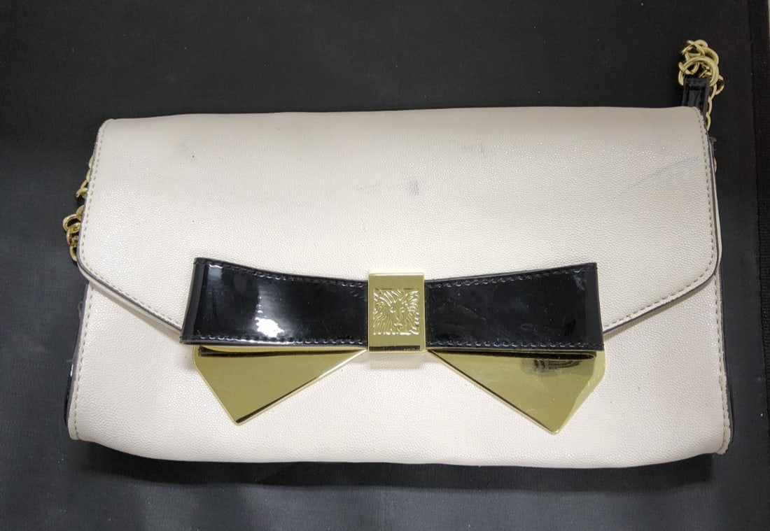 Anne Klein Handbag Shoulder Clutch with Strap Chain & Bow Details: The Anne Klein Handbag Shoulder Clutch is a stylish and versatile accessory for women. Made from faux leather with gold hardware accents, this rectangular shaped clutch features a solid ivory and blac