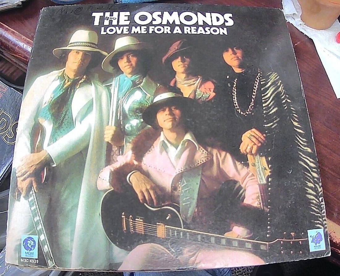 The Osmonds: Love Me For A Reason - MGM Records #M3G4939 - 1974: This 1974 MGM Records 45 RPM single features "Love Me For A Reason" and "Fever" by The Osmonds. The black vinyl record has been graded as Very Good Plus (VG+) and the cardboard sleeve is in Very Good 