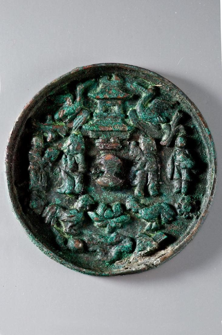 MIRROR WITH PAGODA, BIRDS AND FIGURES: Bronze. China, in the style of Yuan-dynasty Circular form, bowl shape, raised edge. Composition featuring blossoms, birds and human figures, as well as, probably, divinities or fairies in high-relief.