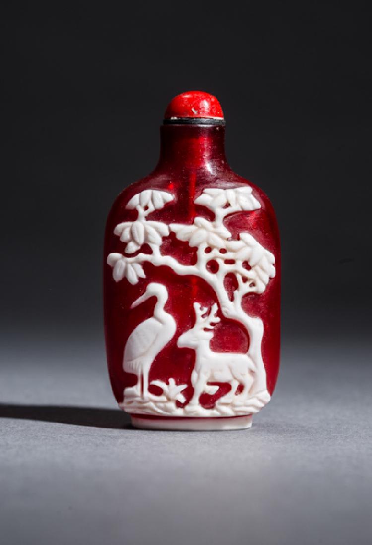 SNUFF BOTTLE WITH PINE TREE, CRANE, STAG, ETC.: Colored cameo glass. China, modern This glowing red snuff bottle shows a crane and deer, two symbols of longevity, underneath a tree on one side, and a bird on a pine tree next to a sitting animal, po