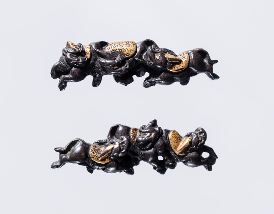 A FINE PAIR OF KIRIN MENUKI: Shakudo with gold. Japan, Edo period Each menuki representing three playful kirin, the saddles, eyes and horns highlighted in gold. Unsigned. Condition: Gilding wear consistent with age - overall good