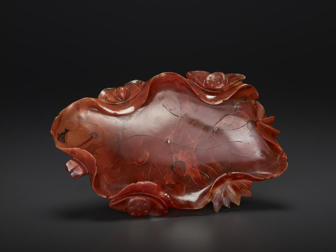 A CARNELIAN AGATE BRUSH WASHER, QING: A CARNELIAN AGATE BRUSH WASHER, QING China, late 18th- 19th century. Cleverly carved as a single lotus leave as the washer, the stems serving as the base and several smaller lotus blossoms on the side