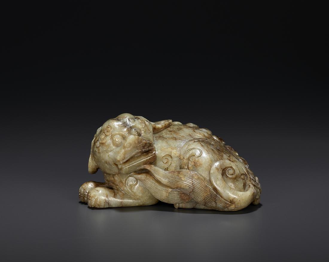 A JADE LION, MING DYNASTY: A JADE LION, MING DYNASTY China, 16th - 17th century. The grey jade with streaks of russet and dark brown. Carved with a recumbent Buddhist lion. Fine detail to fur, tail, and eyebrows. The nostrils d