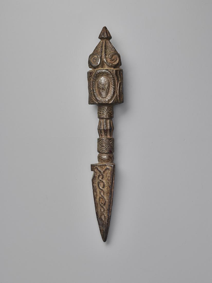 A NEPALESE CARVED WOOD PHURBA: A NEPALESE CARVED WOOD PHURBA Nepal, 17th-19th century. This expressively carved phurba shows an ornate finial and a handle with abstract human masks. Endless knot and intertwined snakes round off the