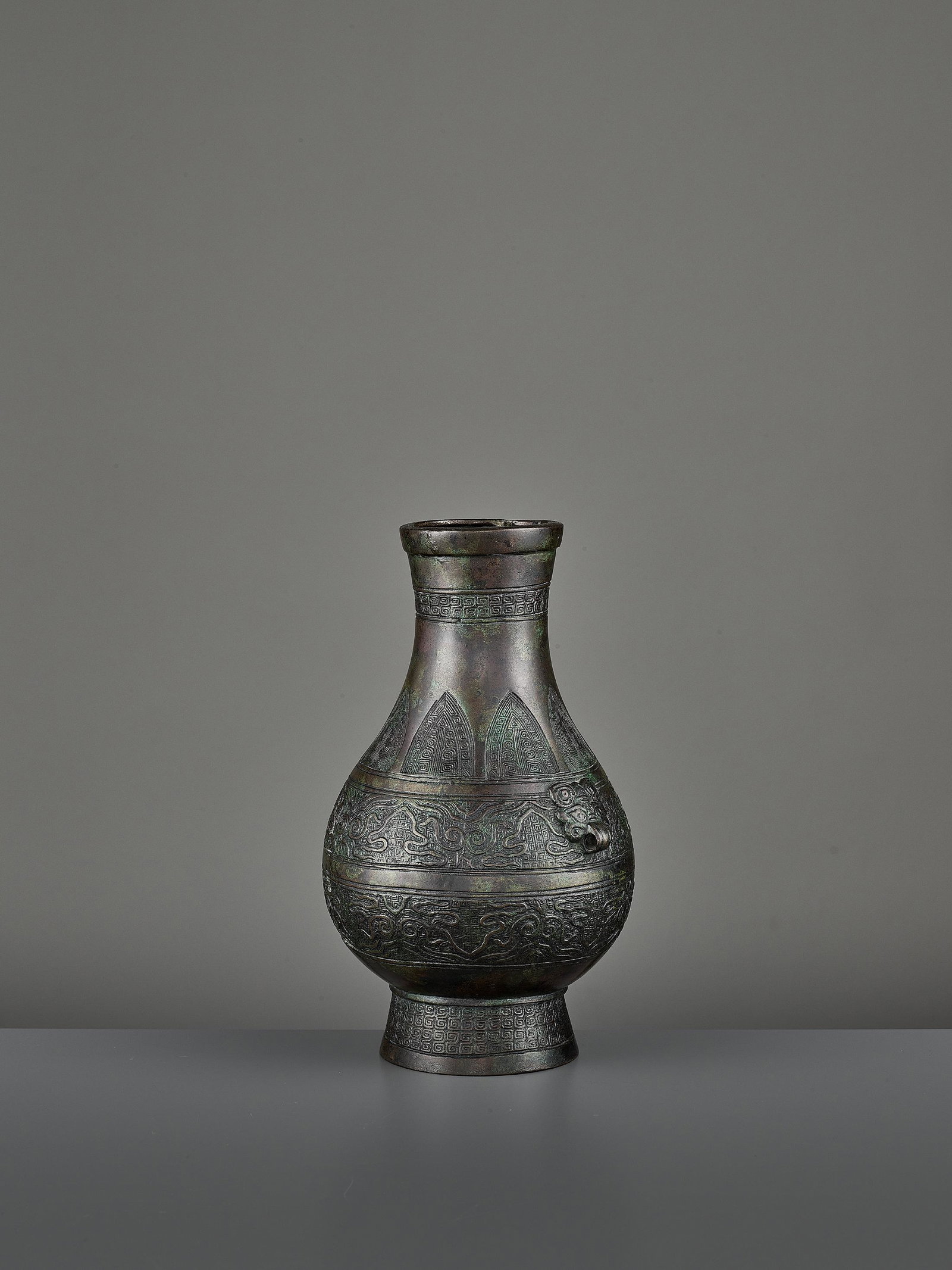 A BRONZE RITUAL VASE, HU: A BRONZE RITUAL VASE, HU China, Ming dynasty (1368-1644) or earlier. The archaistic vessel is cast with a pair of taotie masks and decorated with two archaistic bands below a row of pendant petal-shap