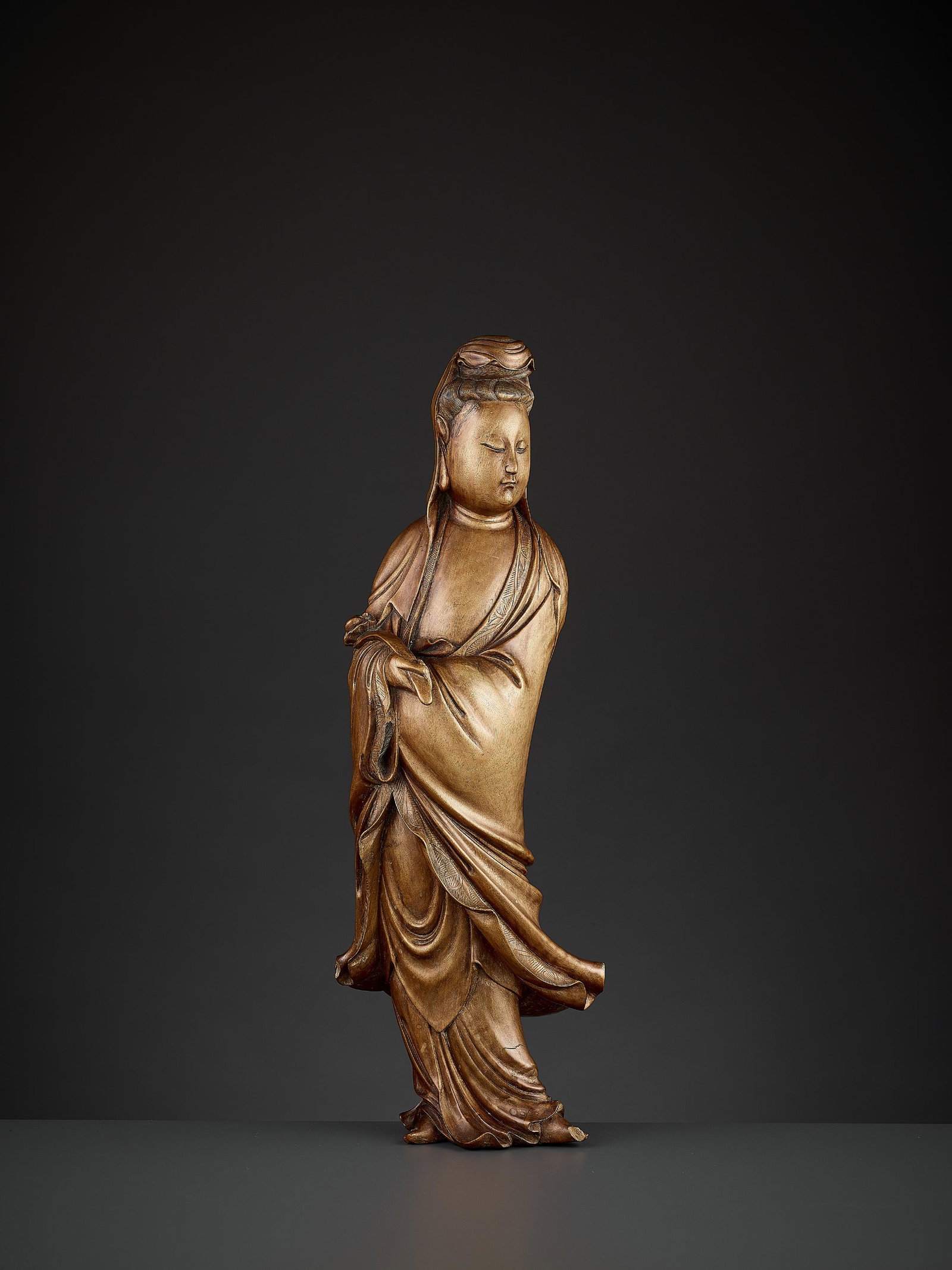 A LARGE BOXWOOD FIGURE OF GUANYIN: A LARGE BOXWOOD FIGURE OF GUANYIN China, 19th century. Carved standing and dressed elegantly in long flowing robes with neatly incised borders, holding a ruyi scepter in the right hand. The face with 