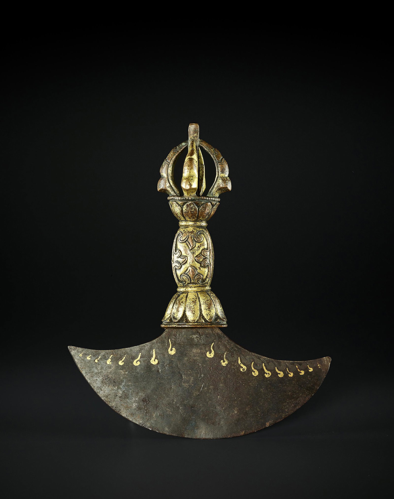 A KARTIKA FLAYING KNIFE, TIBET 17TH CENTURY: A KARTIKA FLAYING KNIFE, TIBET 17TH CENTURY The crescent-shaped iron blade inlaid in gold with wisps of fire, the gilt copper-bronze handle cast as a massive, four-pointed half-vajra, with decor of lo