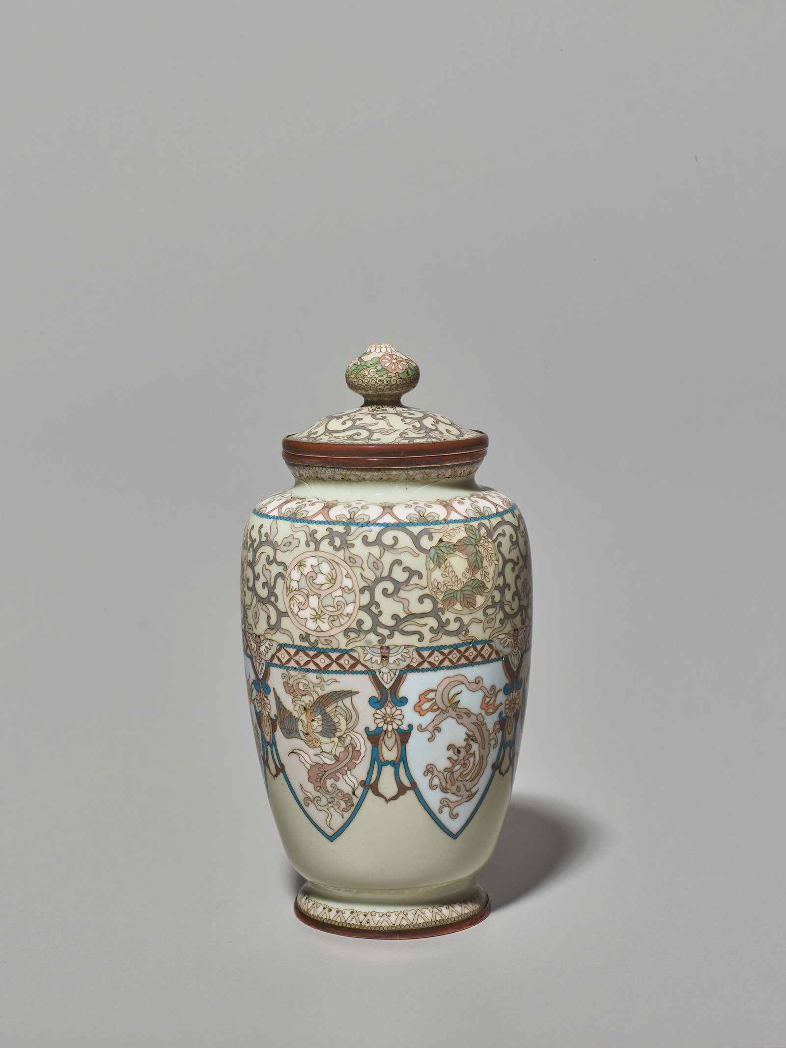 A LIDDED CLOISONNE VASE: A LIDDED CLOISONNE VASE Japan, Meiji period (1868-1912) Baluster shaped vase with a slim body, circular base and lid. The top section is decorated with scrolling vines and floral motifs in circular re