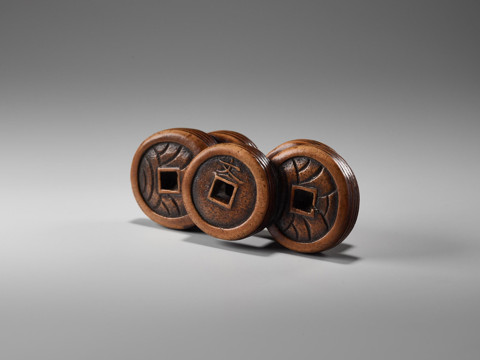 A WOOD NETSUKE OF A GROUP OF COINS: A WOOD NETSUKE OF A GROUP OF COINS Unsigned Japan, 19th century, Edo period (1615-1868) Five piles of five coins each on top of each other with a square hole in the center, except for one group with a