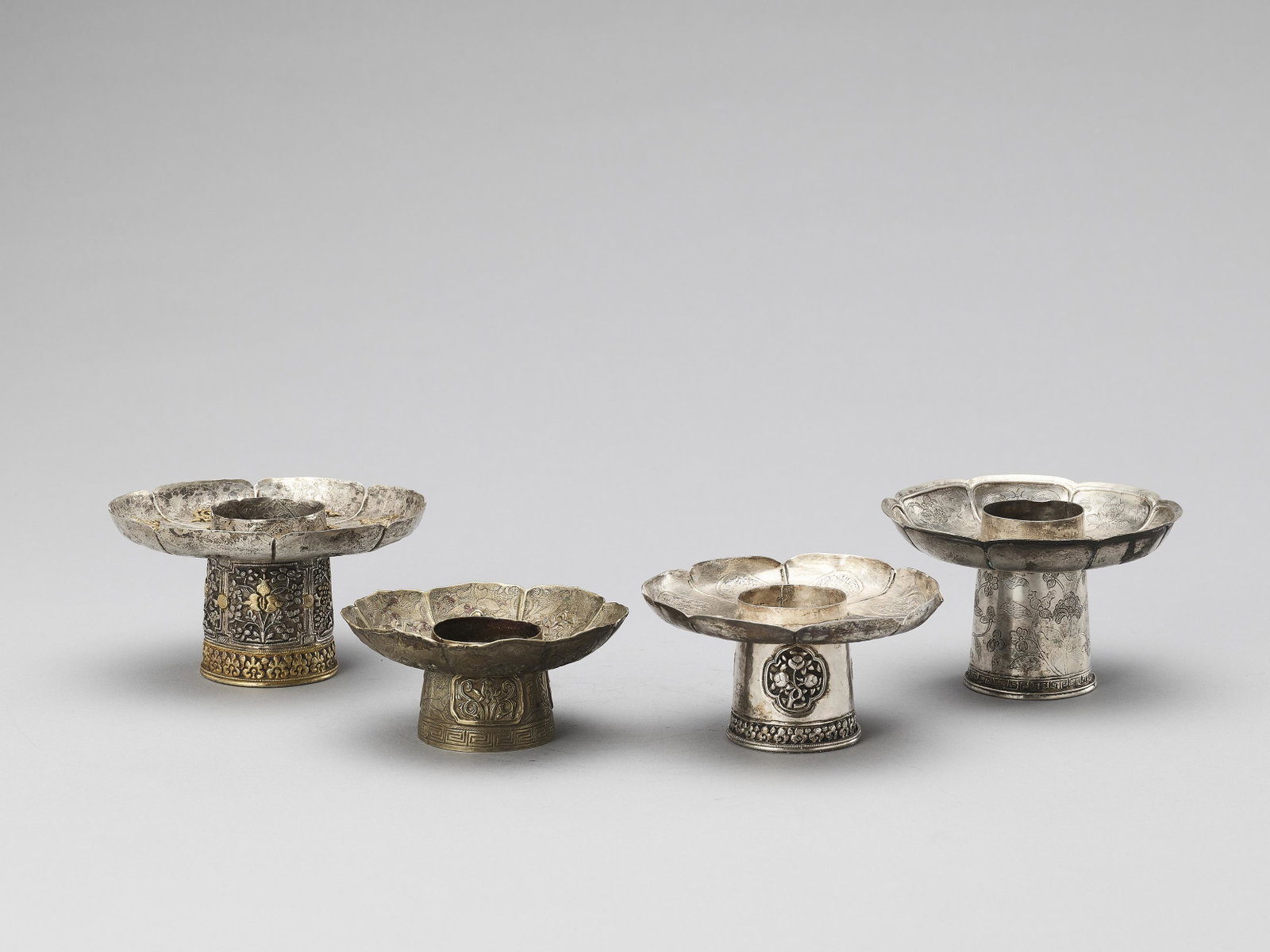 FOUR SINO-TIBETAN SILVER PARCEL-GILT CANDLE HOLDER: FOUR SINO-TIBETAN SILVER PARCEL-GILT 'BAJIXIANG' CANDLE HOLDERS, QING Sino-Tibetean, 18 - 19th century. The foliated, eight-lobed candle holders are engraved or embossed with the Eight Buddhist Symbol