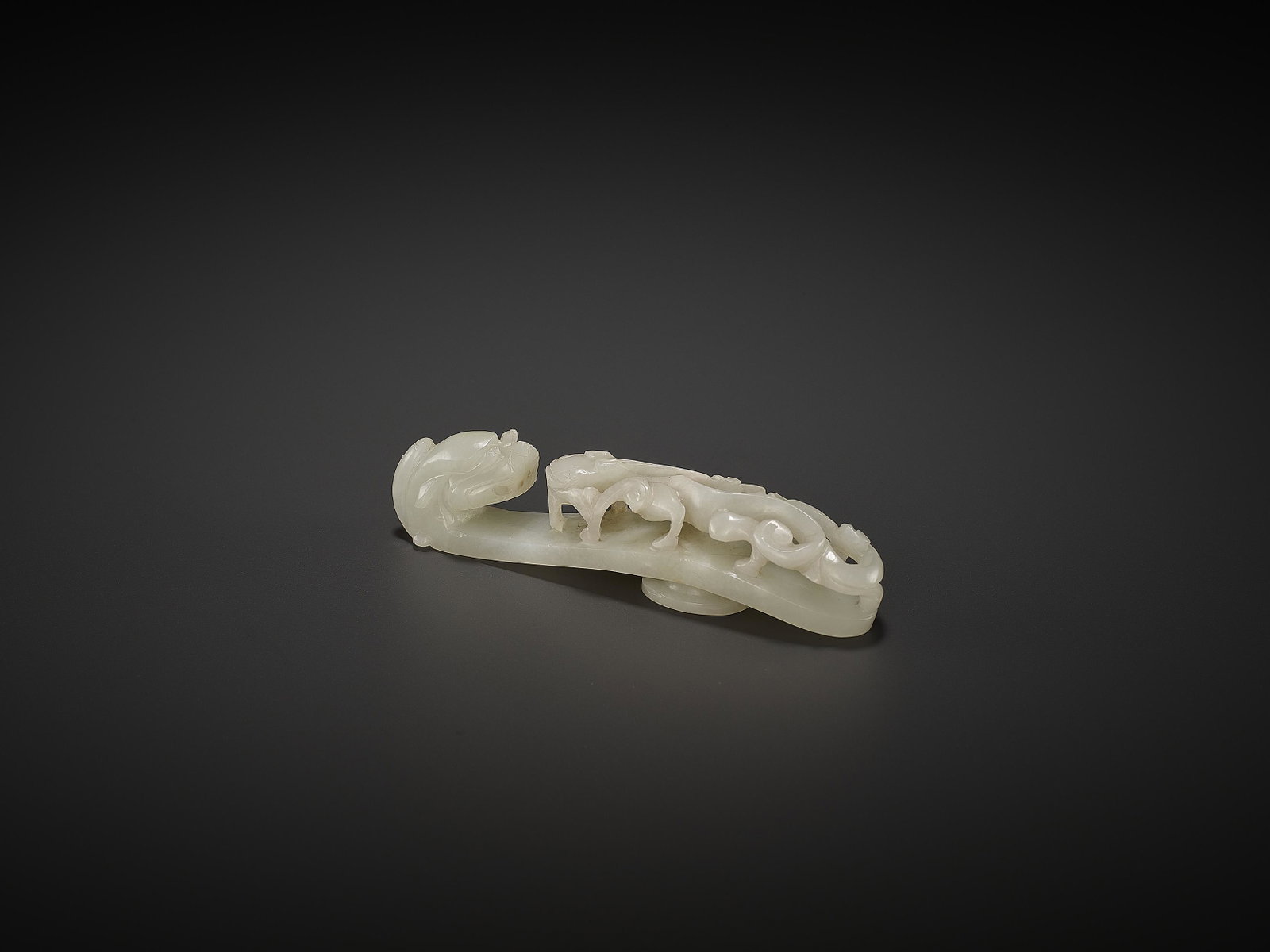 A WHITE JADE BELT HOOK, QING: A WHITE JADE BELT HOOK, QING China, 18th to earlier 19th century. Powerfully worked and incised with a ferocious dragon head terminal facing a chilong in reticulated carving clambering on the curved s
