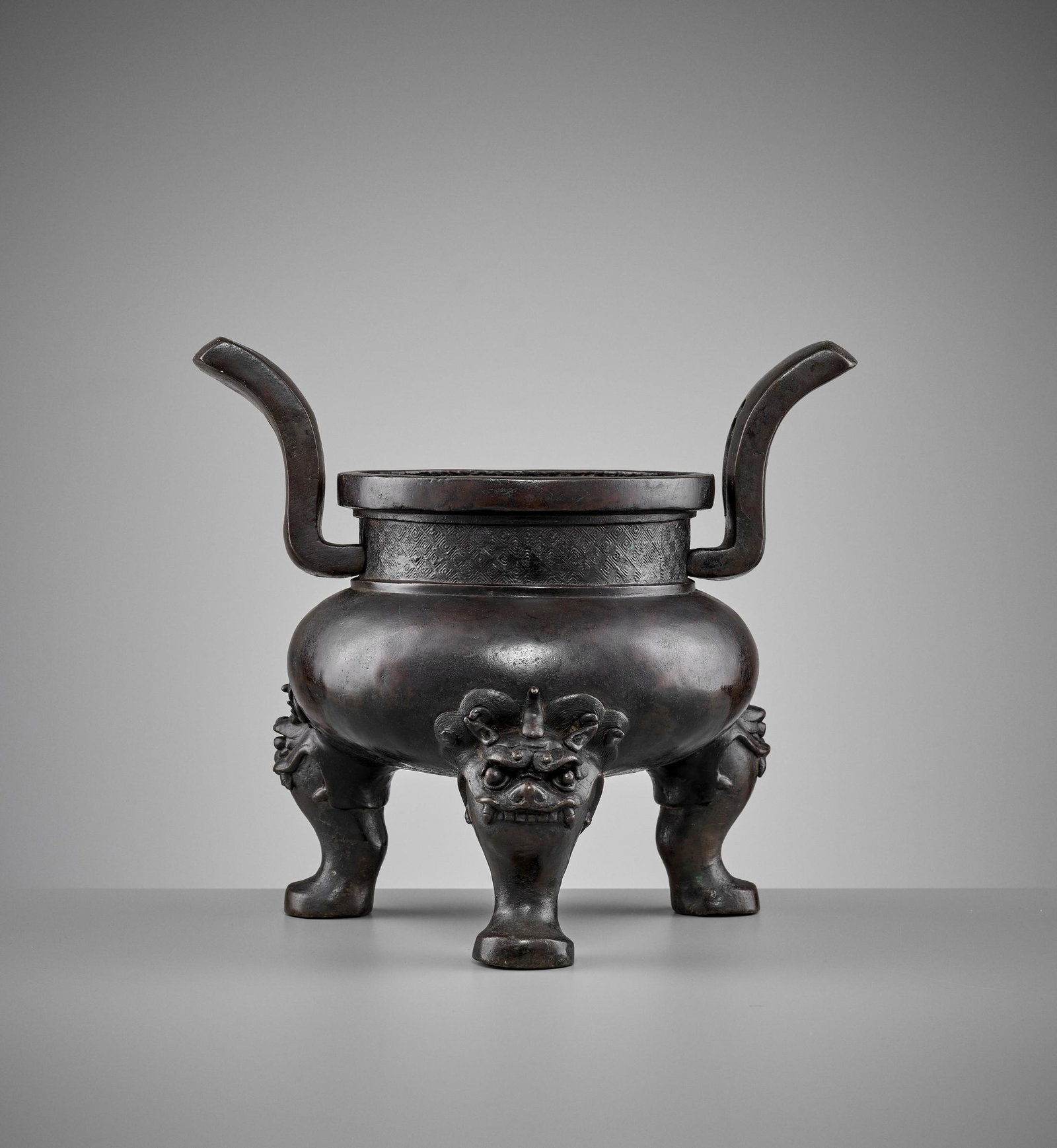 A HEAVILY CAST BRONZE TRIPOD CENSER, MING DYNASTY: A HEAVILY CAST BRONZE TRIPOD CENSER, MING DYNASTY China, 1368-1644. The censer with a compressed globular body raised on three legs issuing from the mouths of horned mythical beasts and a pair of pier