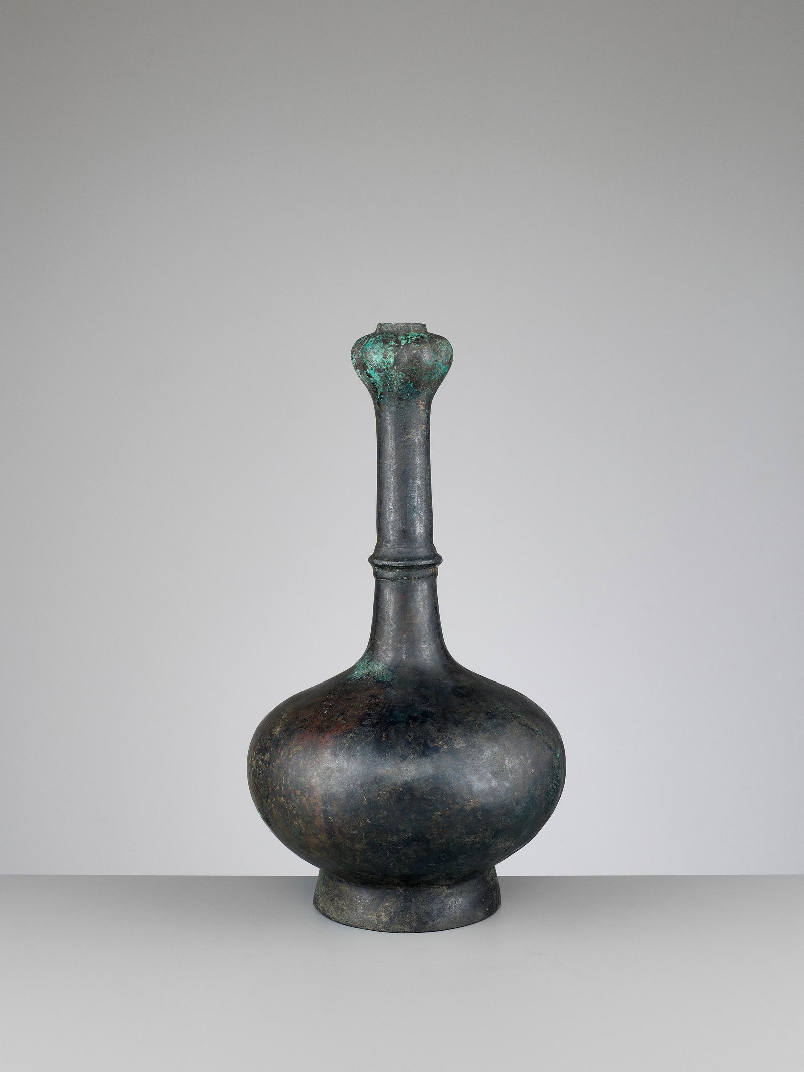 A GARLIC-HEAD BRONZE BOTTLE VASE, HAN DYNASTY: A GARLIC-HEAD BRONZE BOTTLE VASE, HAN DYNASTY China, 206 BC-220 AD. The compressed globular body surmounted by a waisted neck with a raised band at the center and a garlic-head top, all supported on a