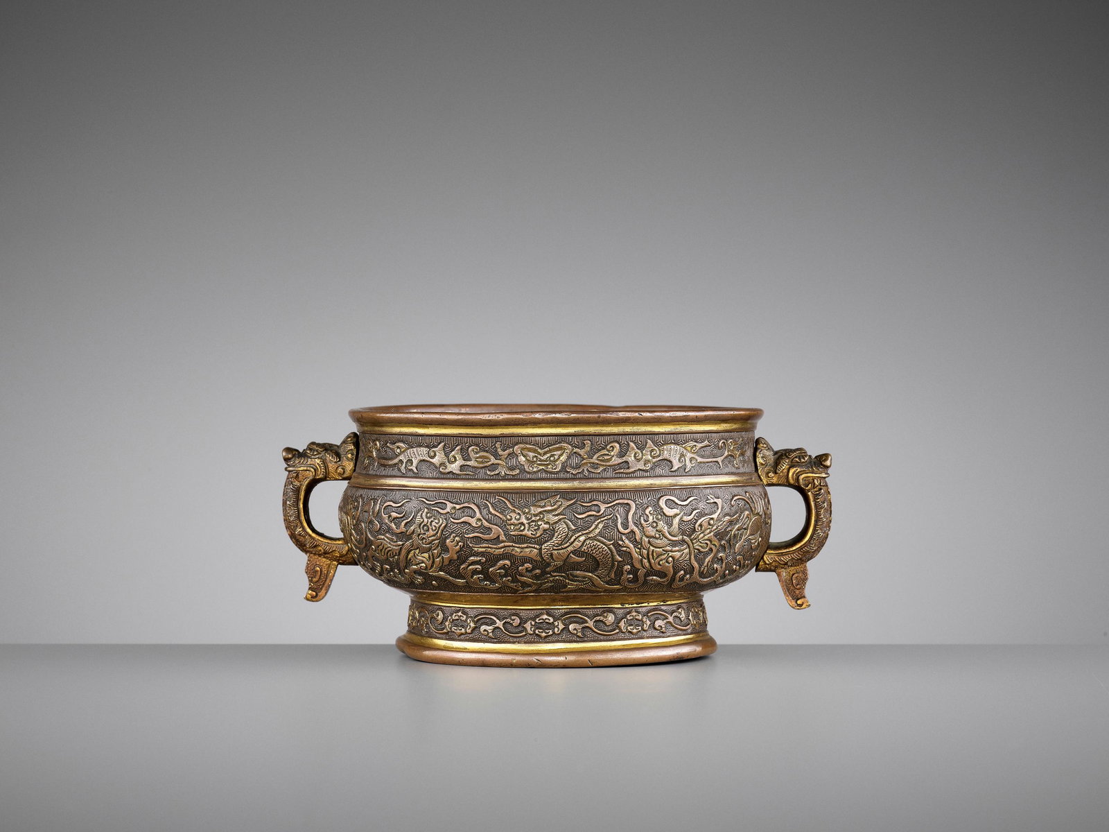 HU WENMING PARCEL-GILT 'DRAGON' CENSER, LATE MING: A HU WENMING PARCEL-GILT 'DRAGON' BRONZE CENSER, LATE MING China, 17th century. Of archaistic gui form, the compressed globular body supported on a splayed lipped foot and flanked by a pair of handles