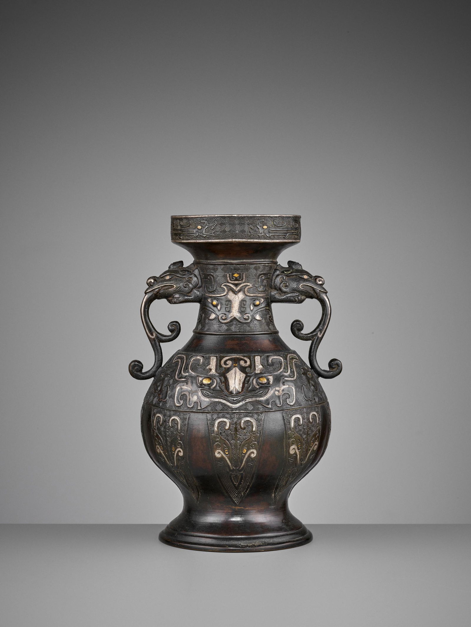 A GOLD AND SILVER INLAID BRONZE VASE, HU, MING: A GOLD AND SILVER INLAID BRONZE VASE, HU, MING DYNASTY China, 16th - 17th century. Heavily cast, the rim decorated with stylized chilong in relief over an incised leiwen band, the neck and body of the