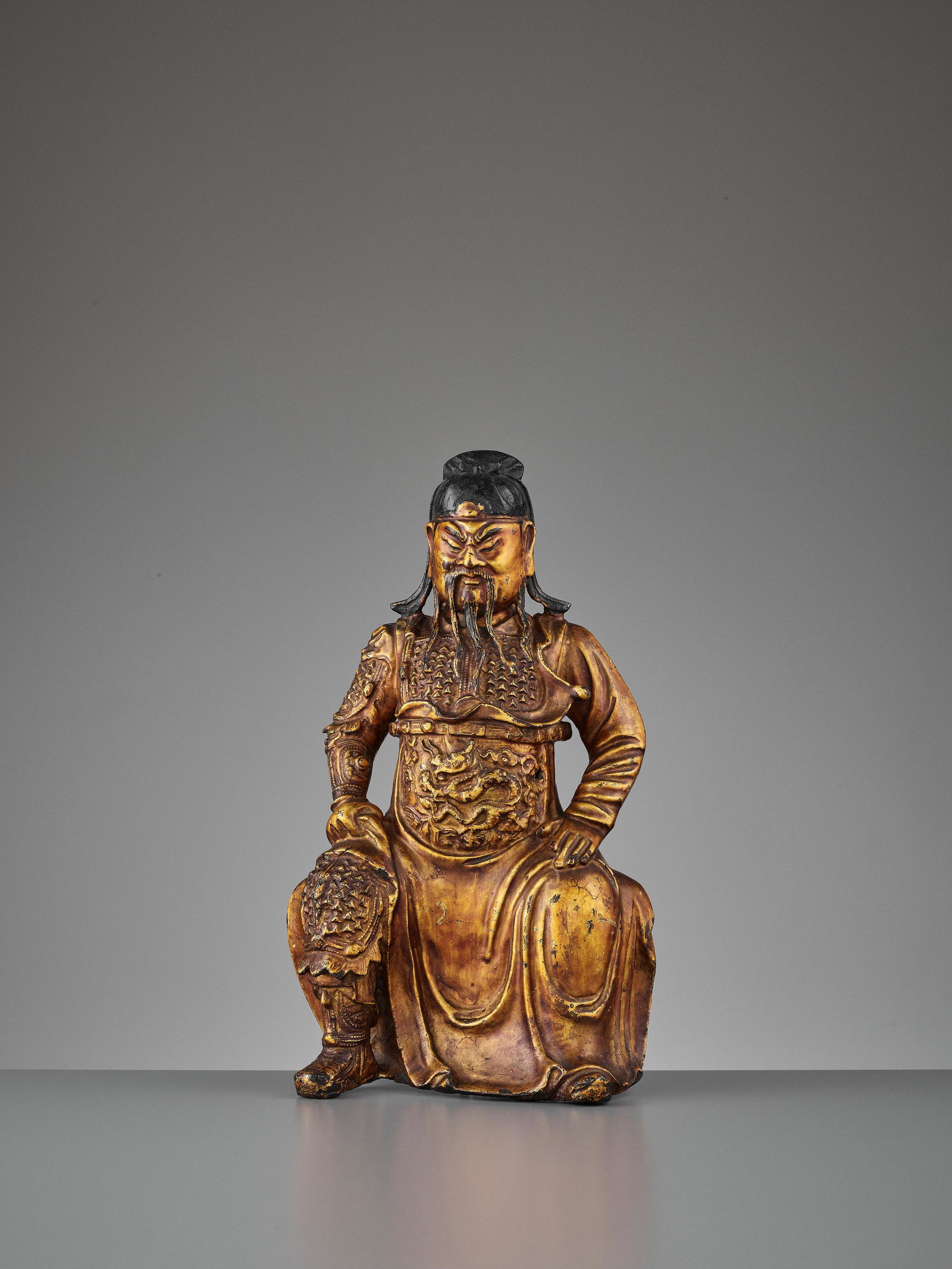 A LACQUER-GILT BRONZE GUANDI, MING DYNASTY: A LACQUER-GILT BRONZE FIGURE OF GUANDI, MING DYNASTY China, 1368-1644. The God of War wearing a finely incised robust armor underneath a long flowing robe decorated in front with a coiled dragon. The 