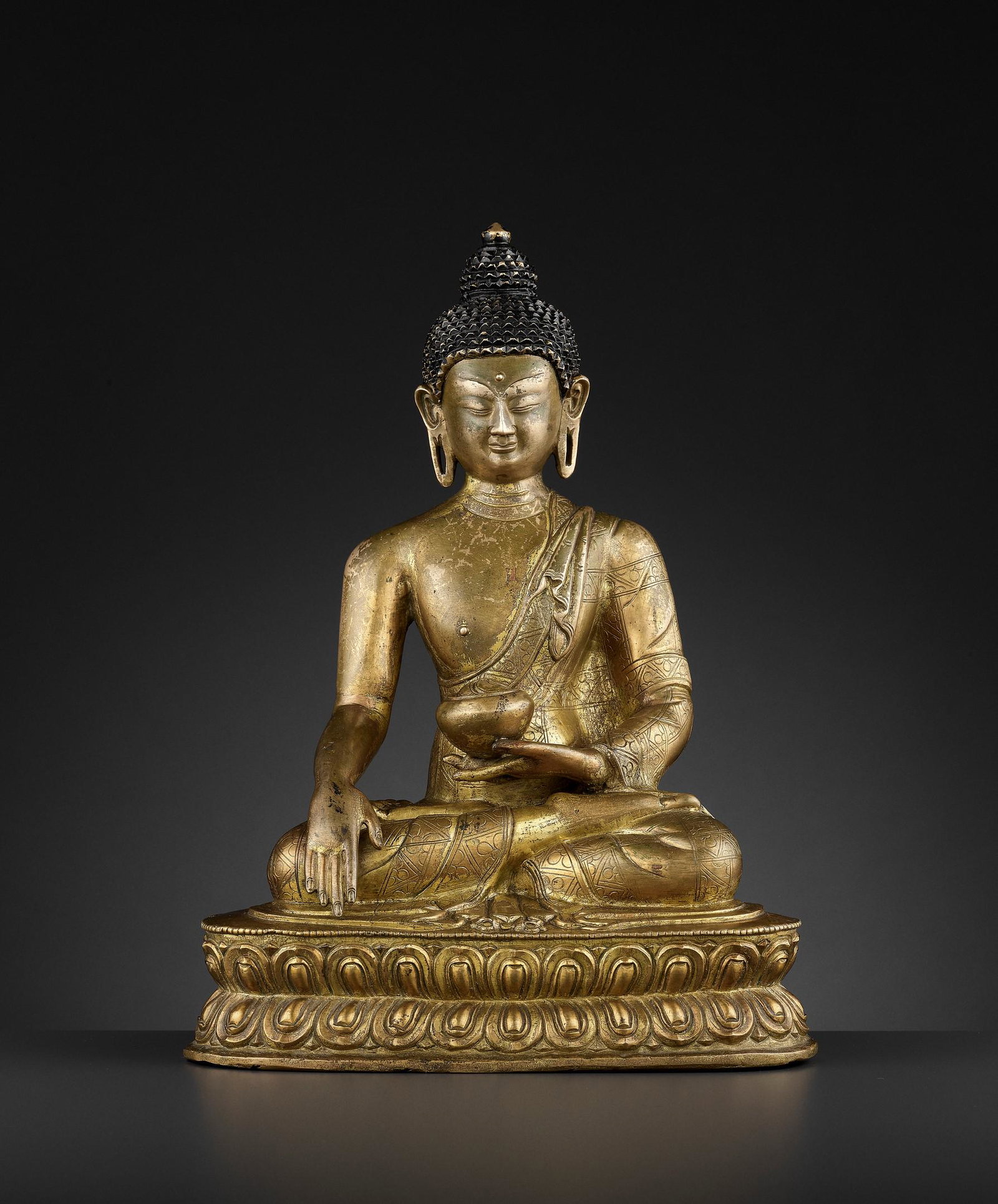 A GILT-BRONZE OF BUDDHA SHAKYAMUNI 17TH CENTURY: A GILT-BRONZE FIGURE OF BUDDHA SHAKYAMUNI, BEIJING OR INNER MONGOLIA, 17TH CENTURY Probably Dolonnor. Finely cast seated in dhyanasana on a raised and beaded double-lotus base, his right hand in bhumi