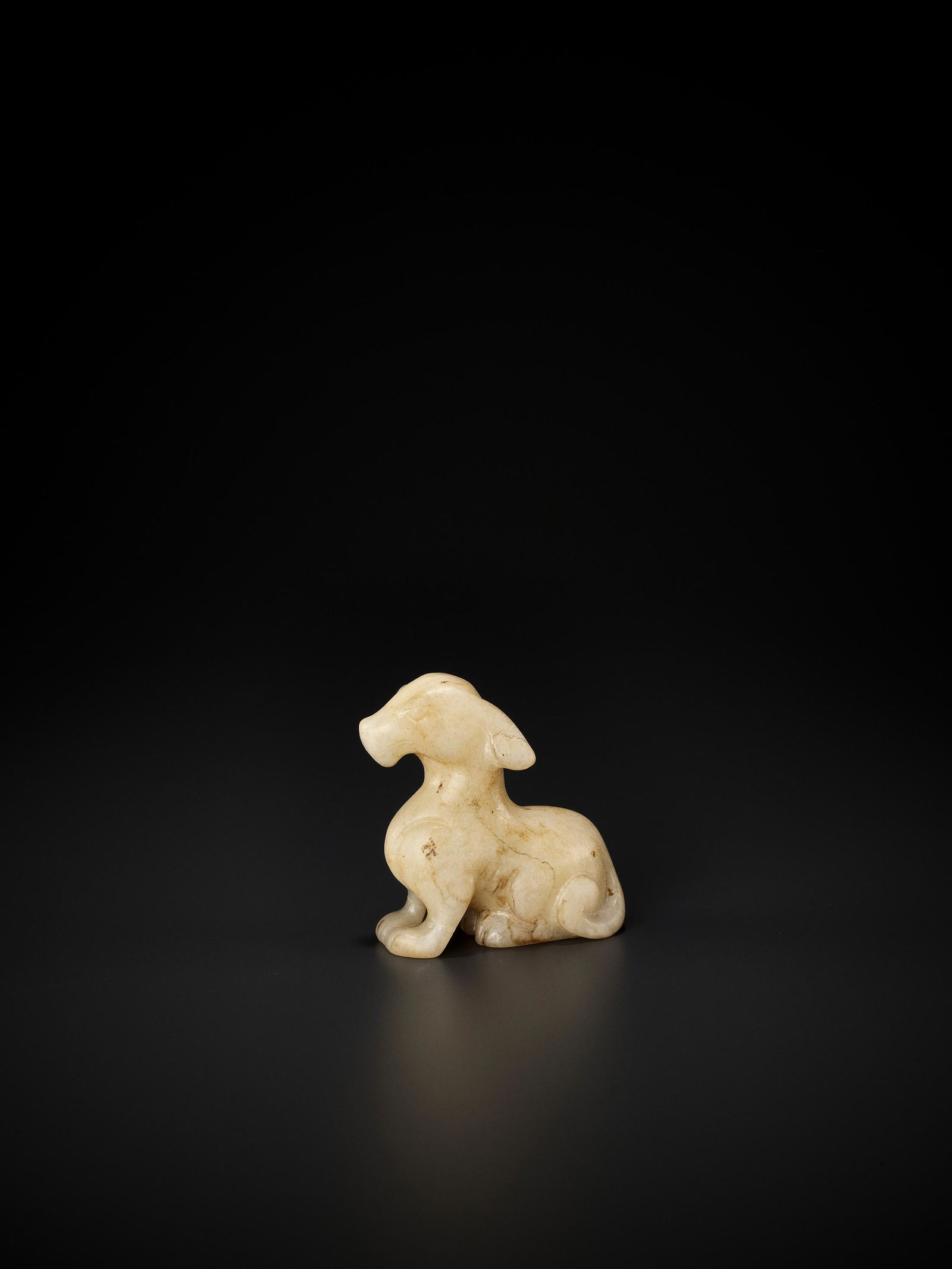 A WHITE JADE SEATED DOG, LATE SONG TO EARLIER MING: A SMALL WHITE JADE FIGURE OF A SEATED DOG, LATE SONG TO EARLIER MING China, 13th-15th century. The opaque stone of an cream-white tone with several russet veins, subtly carved in the form of a seated