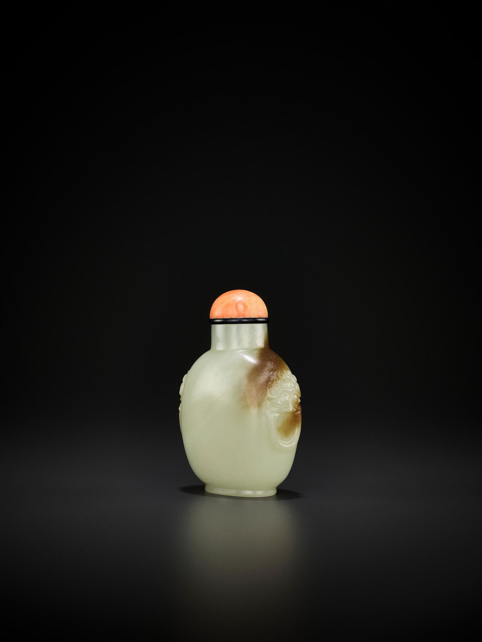 A CELADON AND RUSSET JADE SNUFF BOTTLE, MID-QING: A CELADON AND RUSSET JADE 'LION MASK' SNUFF BOTTLE, MID-QING China, 1750-1850. Well-hollowed, of rounded rectangular form with an oval foot rim and short cylindrical neck, the shoulders carved in reli