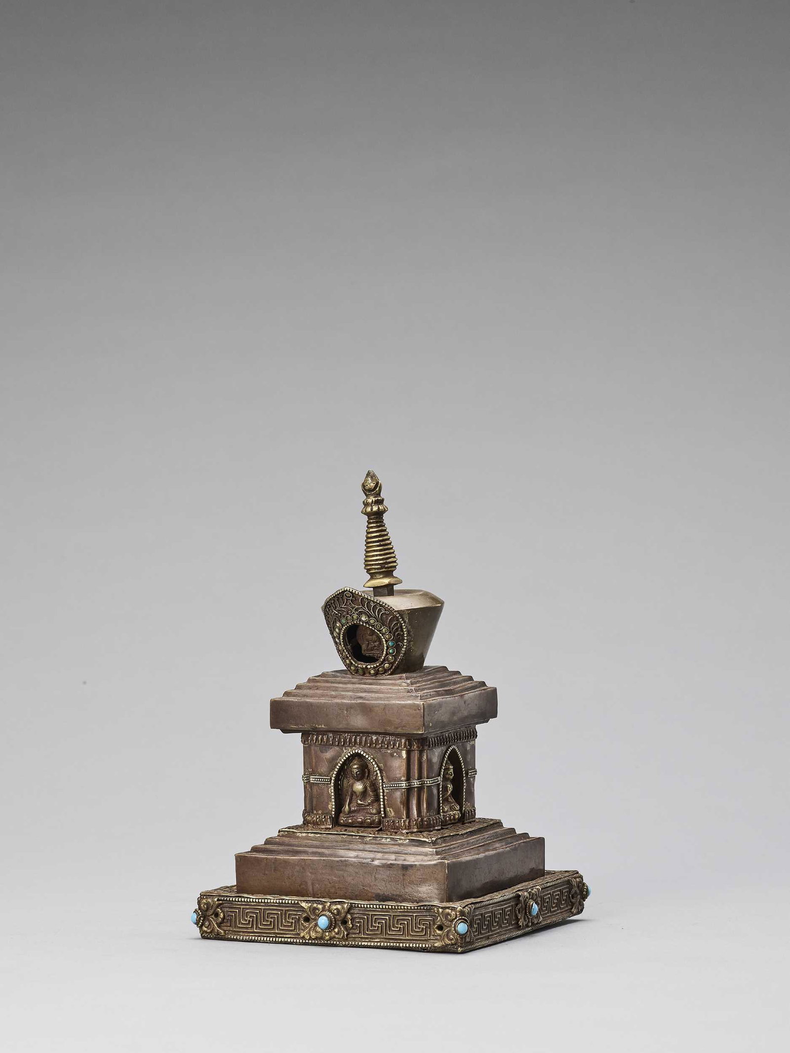 A TIBETAN COPPER REPOUSSE STUPA WITH TURQUOISES: A TIBETAN COPPER REPOUSSE STUPA WITH TURQUOISES, 19TH CENTURY Tibet. The bumpa decorated with inlaid turquoises and gold foil, a terracotta tsa-tsa of Buddha inside, above four niches with Buddha figu