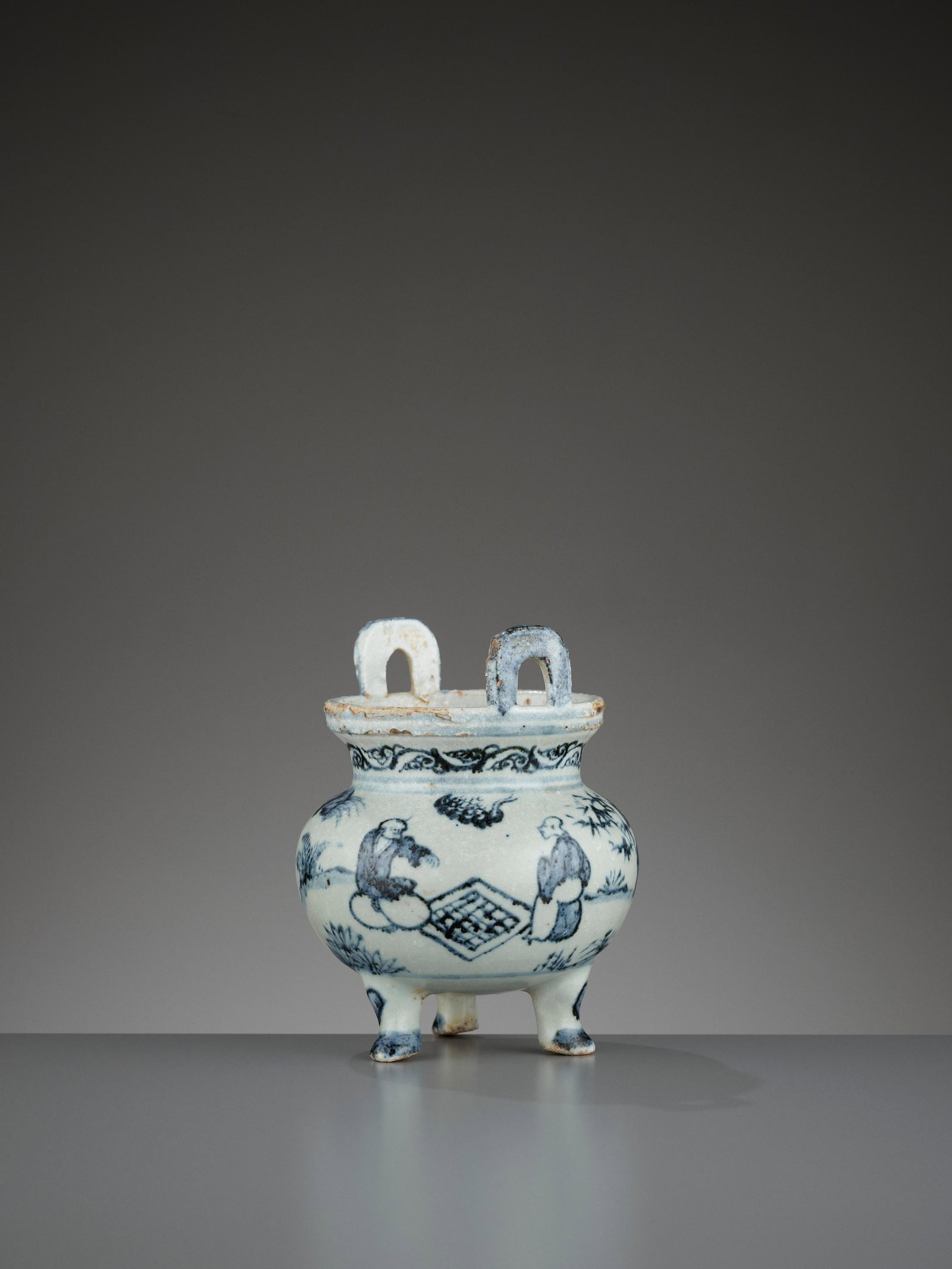 A 'WEIQI PLAYERS' BLUE AND WHITE PORCELAIN CENSER, MING: A 'WEIQI PLAYERS' BLUE AND WHITE PORCELAIN TRIPOD CENSER, MING DYNASTY China, 1368-1644. The compressed globular vessel is supported on three feet, rising to a short cylindrical neck and a cupped rim 