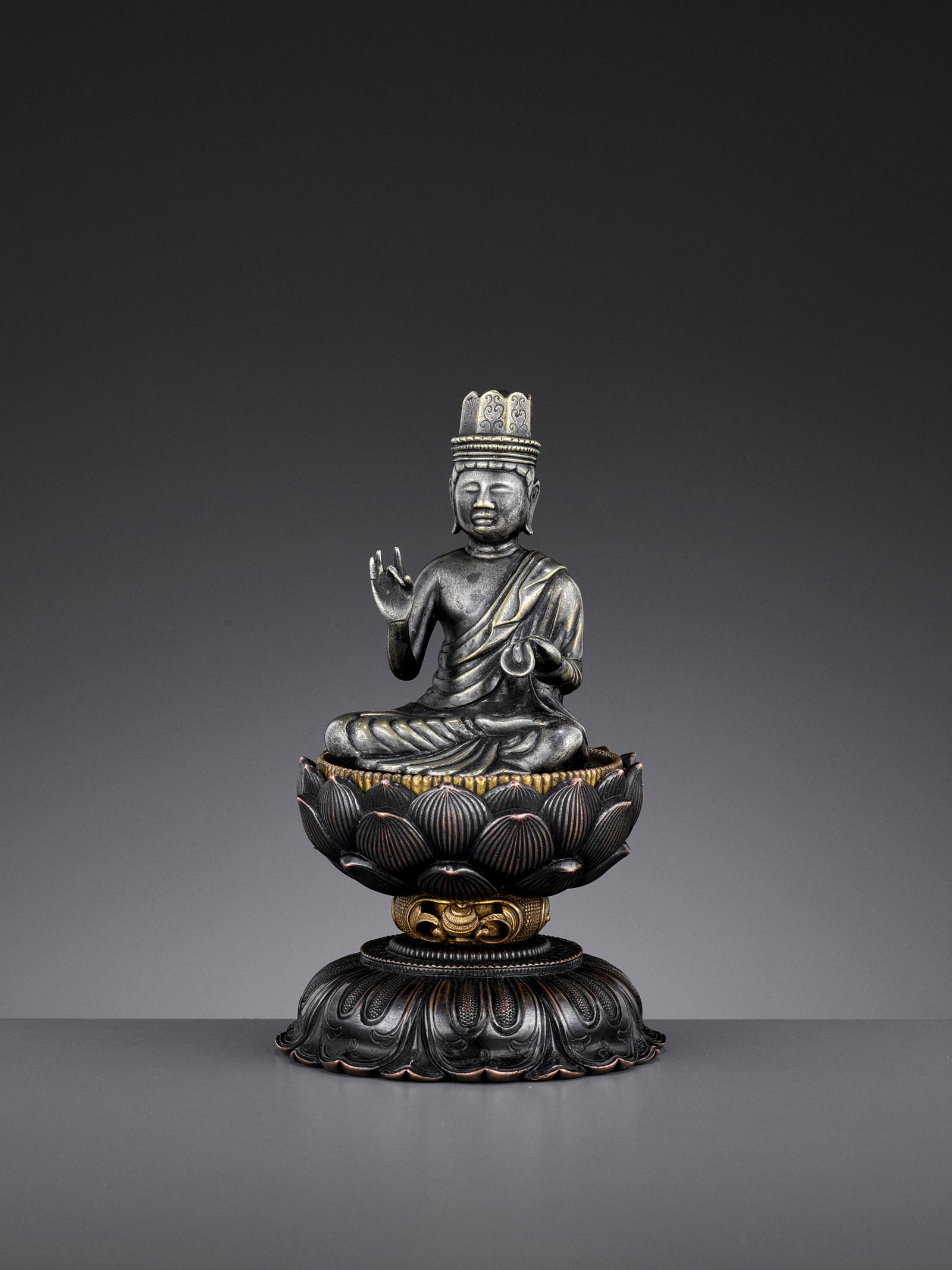 A KOREAN PARCEL-GILT AND SILVERED CROWNED BUDDHA, 19TH: A KOREAN PARCEL-GILT AND SILVERED METAL FIGURE OF A CROWNED BUDDHA, 19TH CENTURY Seated in dhyanasana on a separately cast lotus base, the right hand raised in vitarka mudra and the left holding the h