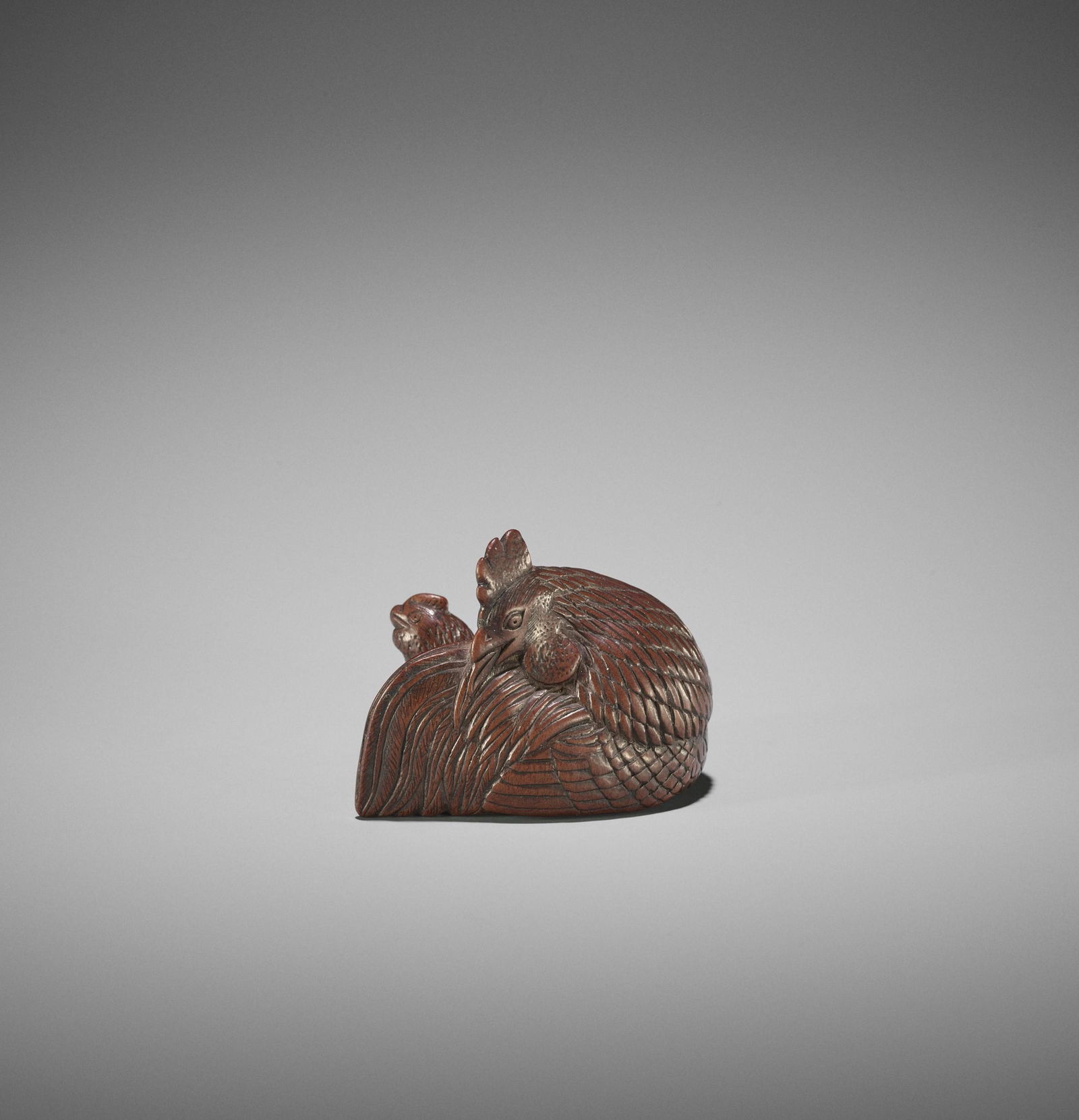 A SUPERB WOOD NETSUKE OF A COCKEREL AND HEN: A SUPERB WOOD NETSUKE OF A COCKEREL AND HEN UnsignedJapan, possibly Kyoto, late 18th century, Edo period (1615-1868)The rooster and hen resting side by side, the large and proud male with long tail fe