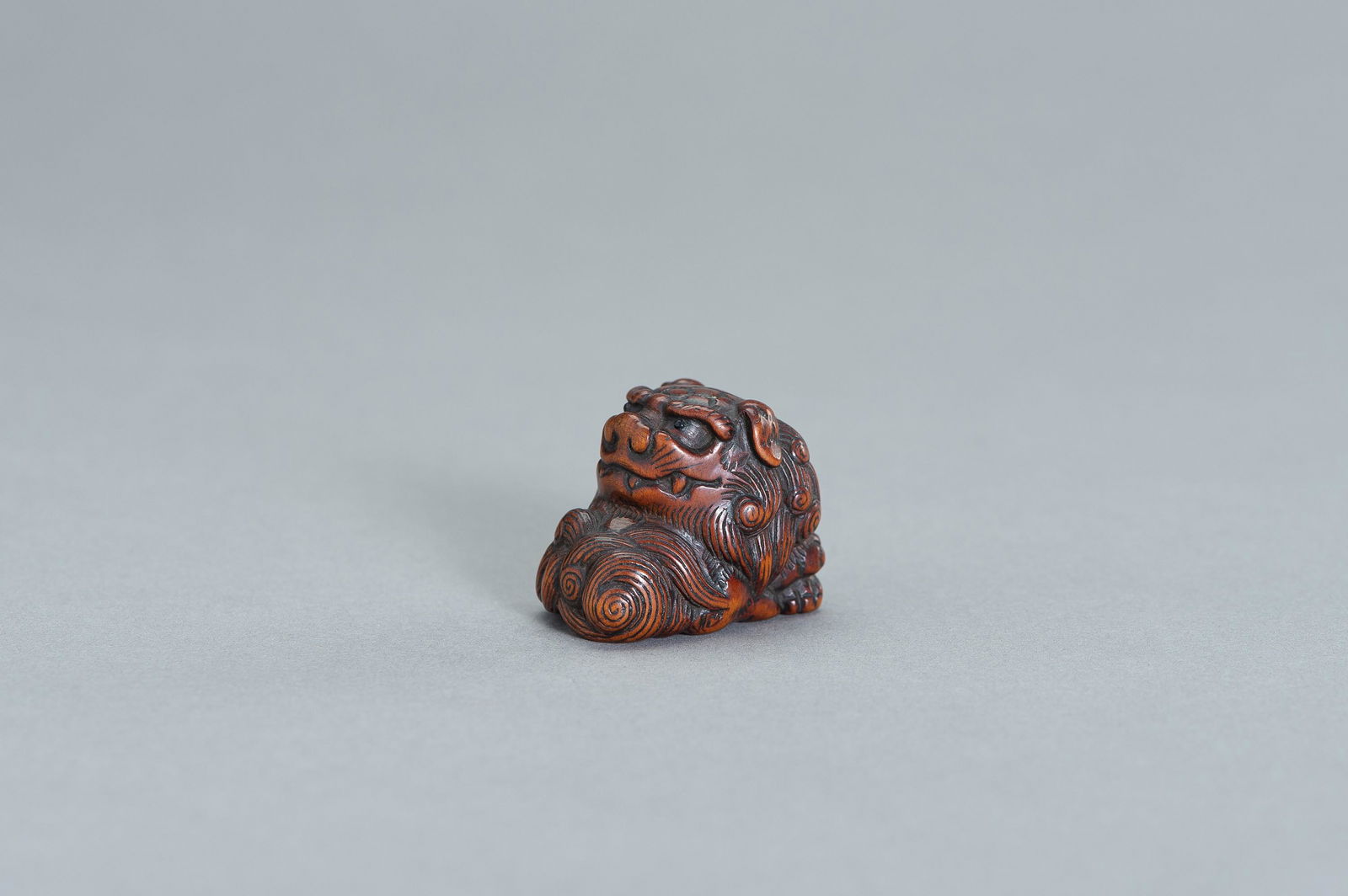 YOSHINOBU: A WOOD NETSUKE OF A RECLINING SHISHI (1 of 10)