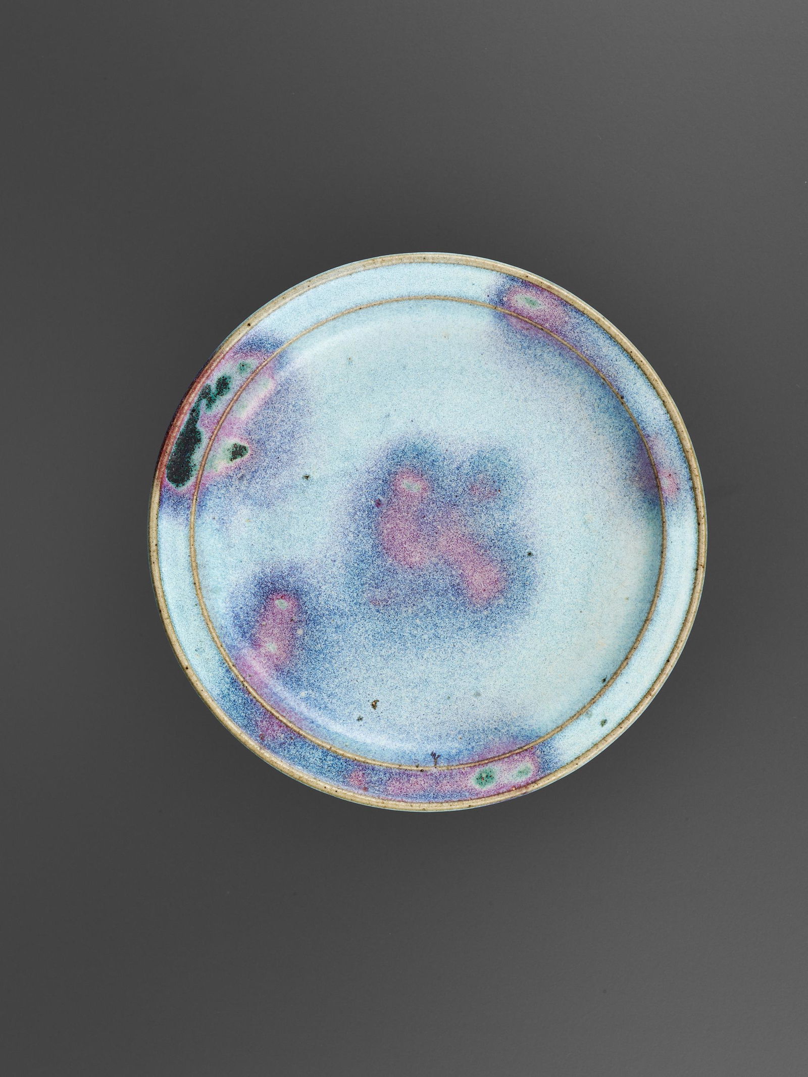 A PURPLE-SPLASHED JUN-GLAZED DISH, JIN DYNASTY: A PURPLE-SPLASHED JUN-GLAZED DISH, JIN DYNASTY China, 1115-1234. The low rounded sides rising from a short foot to an everted rim with a finely raised lip. The interior decorated with distinct purple