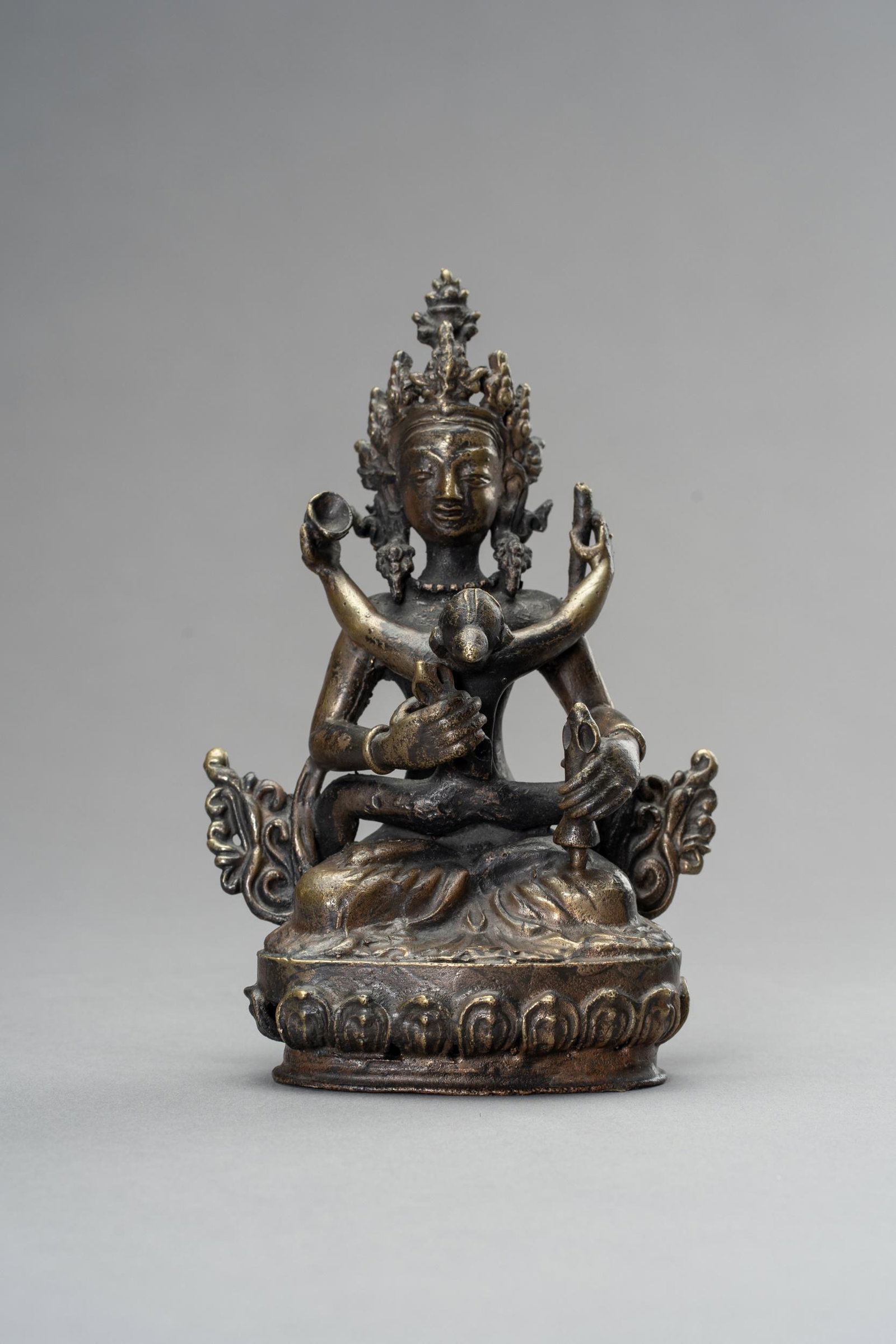 A BRONZE GROUP OF VAJRASATTVA & VAJRAMAMANI, 1900: A BRONZE GROUP OF VAJRASATTVA IN UNION WITH VAJRAMAMANI, 1900s Nepal, late 19th to early 20th century. The deity cast seated in dhyanasana upon a lotus pedestal embracing his consort in yab-yum, his h