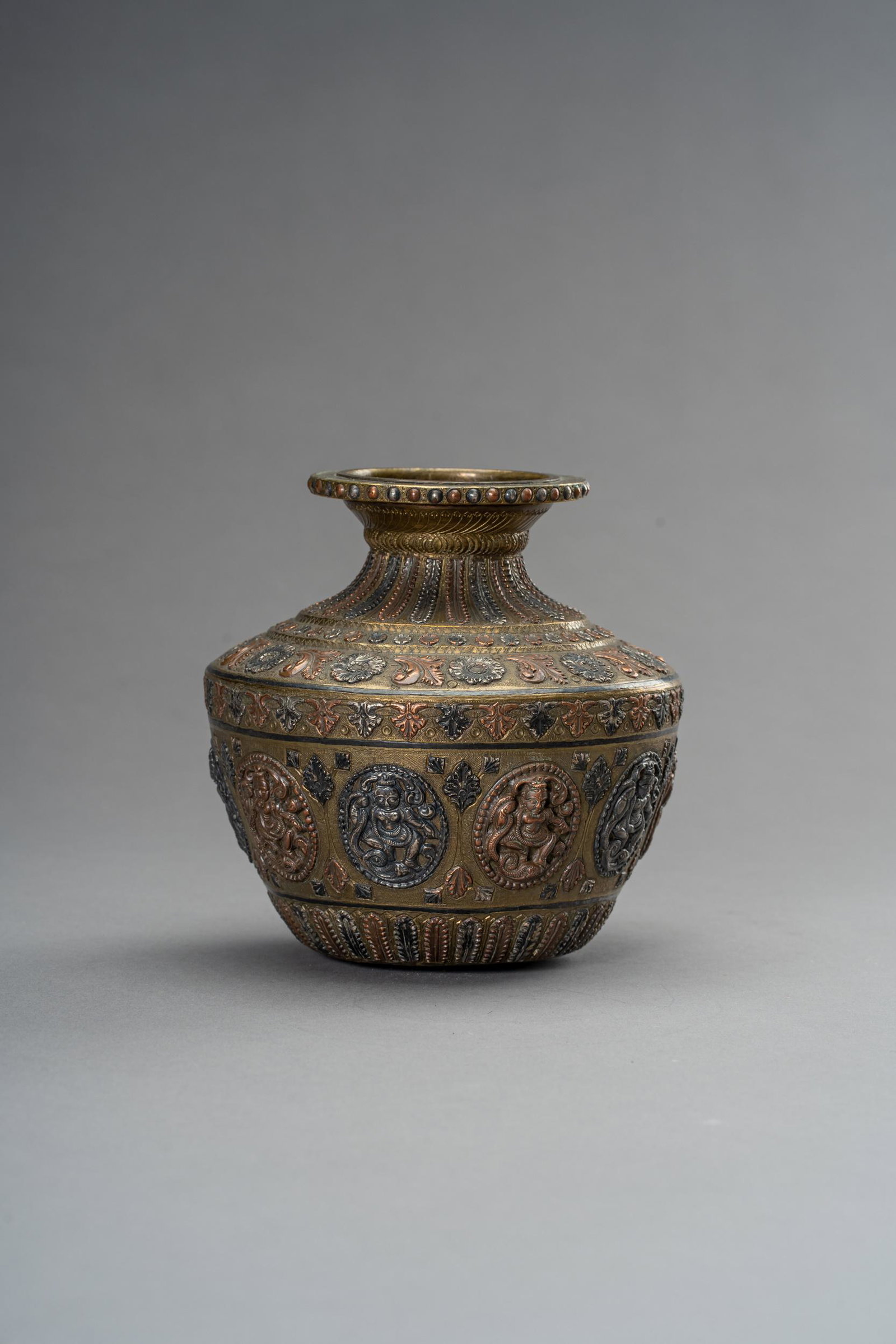 A MIXED-METAL LOTA VESSEL, 1900s: A MIXED-METAL LOTA VESSEL, 1900s Nepal, late 19th to early 20th century. The round-bellied brass vessel with silver and copper applications, depicting several reserves with deities and naga, the neck 