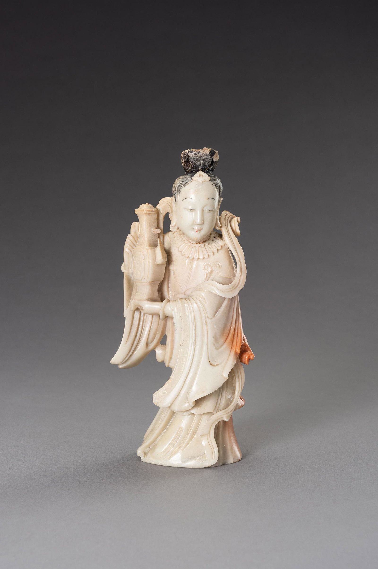 A CARVED SOAPSTONE FIGURE OF A LADY, 1900s: A CARVED SOAPSTONE FIGURE OF A LADY, 1900s China, late Qing dynasty (1644-1912) - Republic period (1912-1949). The figure is shown standing and holding a large teapot in both her hands. She wears a sh