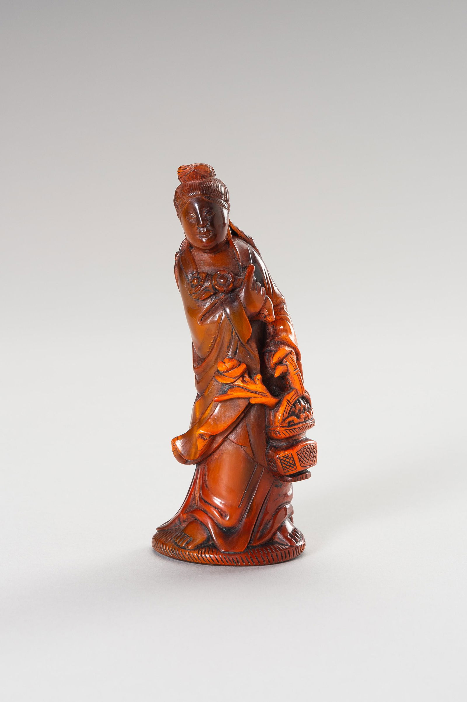 A HORN FIGURE OF GUANYIN: A HORN FIGURE OF GUANYIN China, Qing Dynasty (1644-1912). Guanyin carved leaning towards her right side, dressed in a long robe and holding a flower basket in her left hand and a flowering branch in h