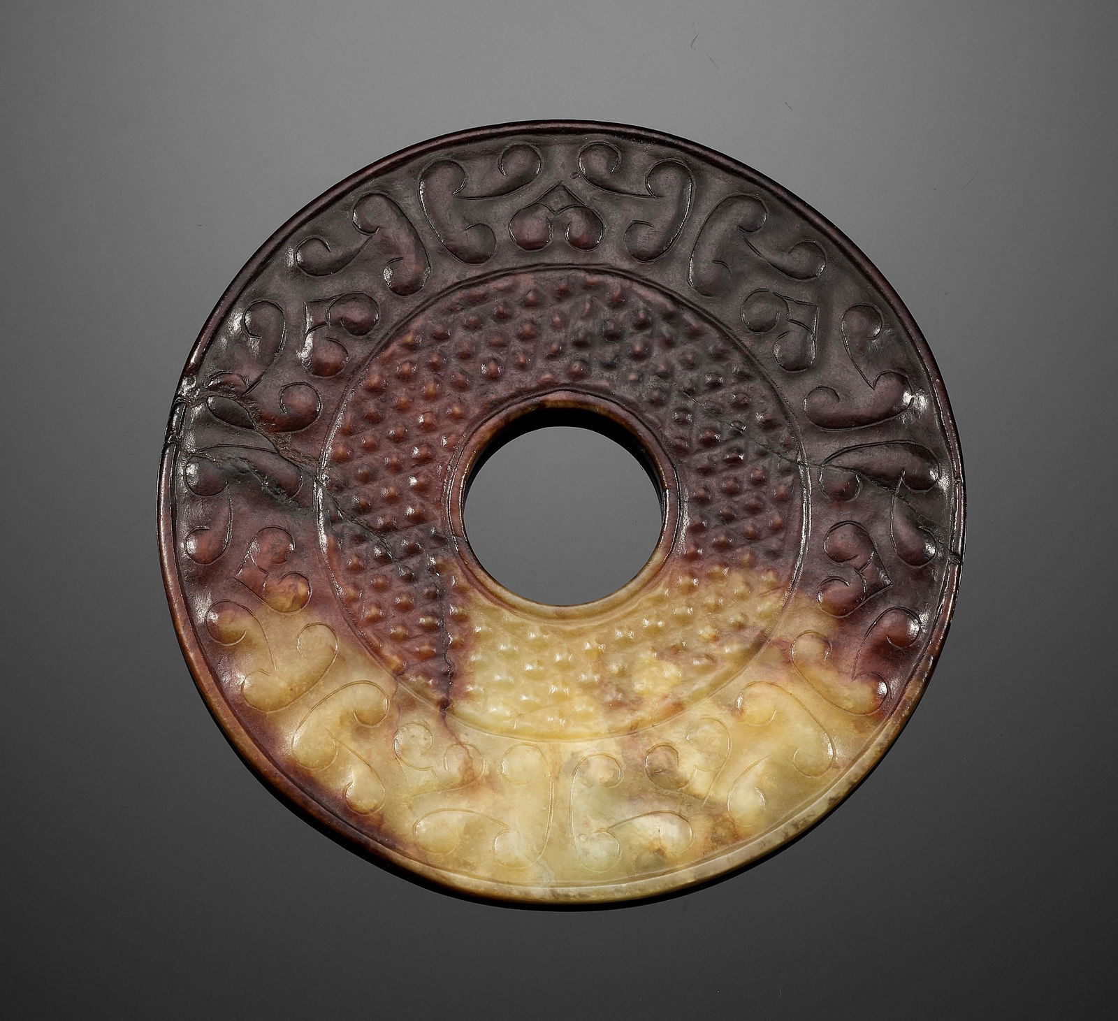 AN ARCHAISTIC PALE CELADON AND DARK RUSSET JADE BI DISC: AN ARCHAISTIC PALE CELADON AND DARK RUSSET JADE BI DISC China, Qing Dynasty (1644-1912) or earlier. The inner area is decorated with a pattern of densely arranged nodes reminiscent of guwen (comma spi