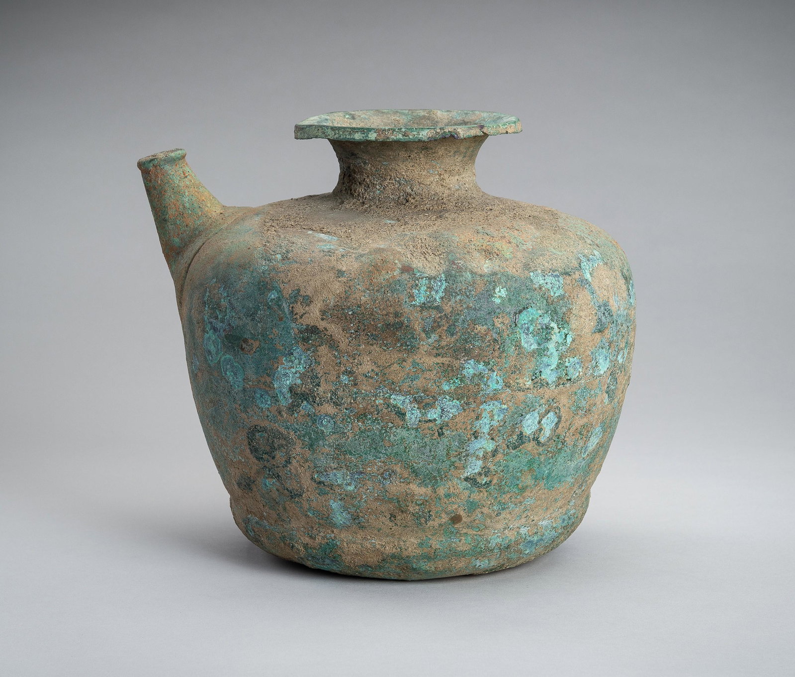 A HAN STYLE BRONZE POURING VESSEL: A HAN STYLE BRONZE POURING VESSEL China, presumably Han Dynasty or later. Of compressed baluster form with a short neck and flaring mouth, cast to one side with a spout pierced with seven small openin