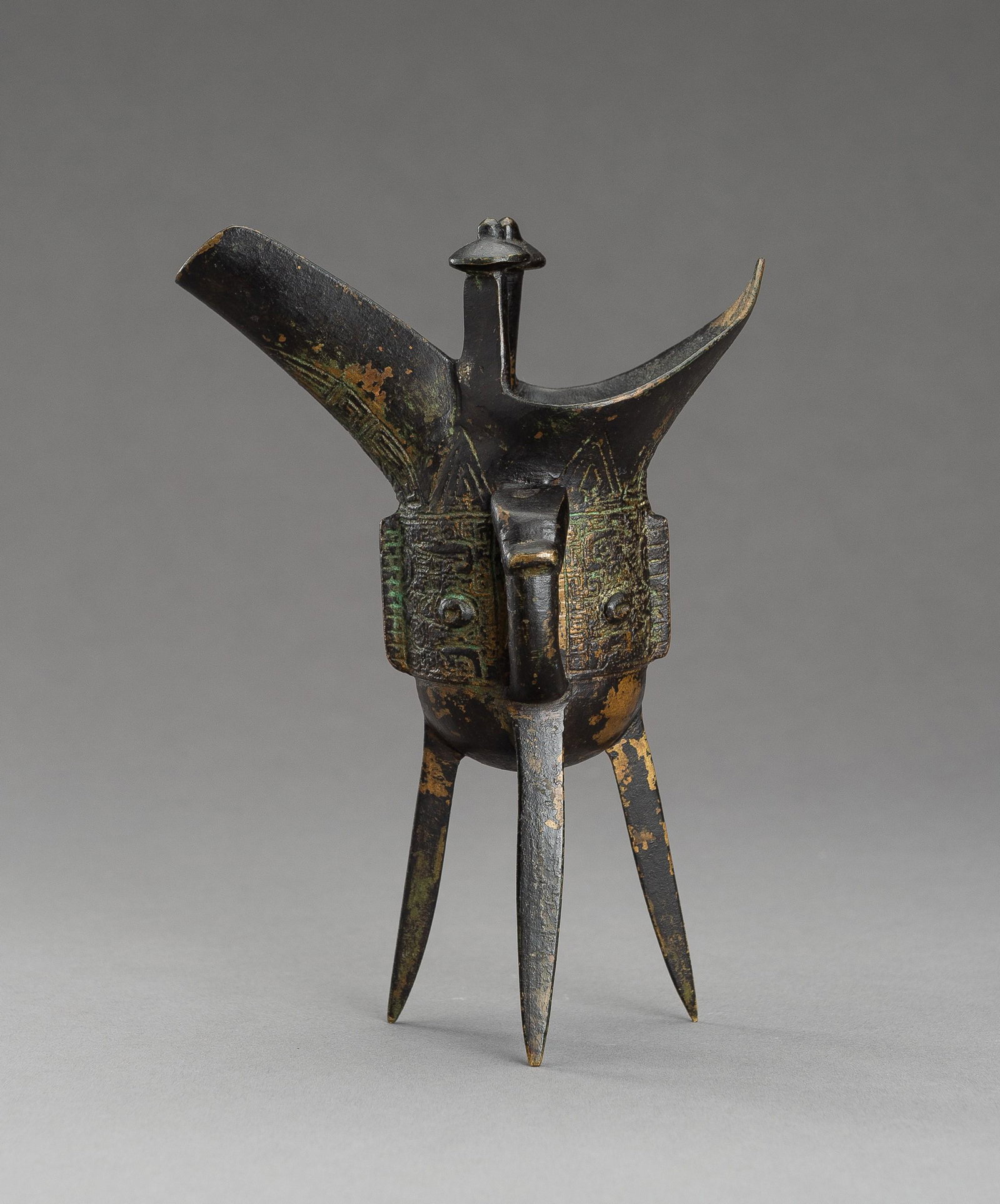 AN ARCHAISTIC SHANG STYLE BRONZE RITUAL TRIPOD WINE VESSEL, JUE: AN ARCHAISTIC SHANG STYLE BRONZE RITUAL TRIPOD WINE VESSEL, JUE China, late Ming Dynasty (1368-1644) to early Qing Dynasty (1644-1912), 17th century. The tripod vessel raised on three tall blade-shape