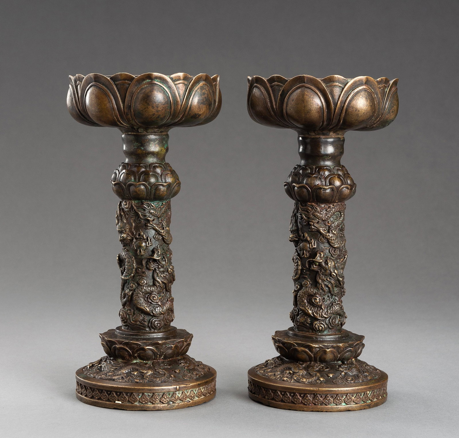 A PAIR OF ARCHAISTIC BRONZE CANDLE HOLDERS, 1900s: A PAIR OF ARCHAISTIC BRONZE CANDLE HOLDERS, 1900s China, late Qing dynasty (1644-1912) to Republic period (1912-1949). Raised on a circular plinth surmounted by a lotus flower, the cup also in shape o