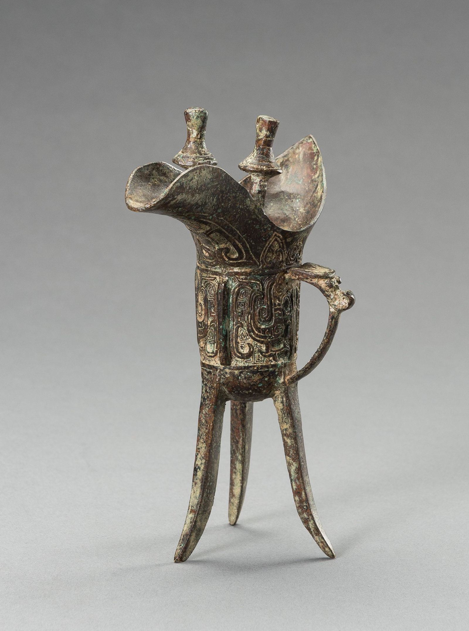 AN ARCHAISTIC SHANG-STYLE BRONZE RITUAL TRIPOD WINE VESSEL, JUE: AN ARCHAISTIC SHANG-STYLE BRONZE RITUAL TRIPOD WINE VESSEL, JUE China, late Qing Dynasty (1644-1912) to Republic period (1912-1949). The tripod vessel raised on three tall blade-shaped feet and cast w