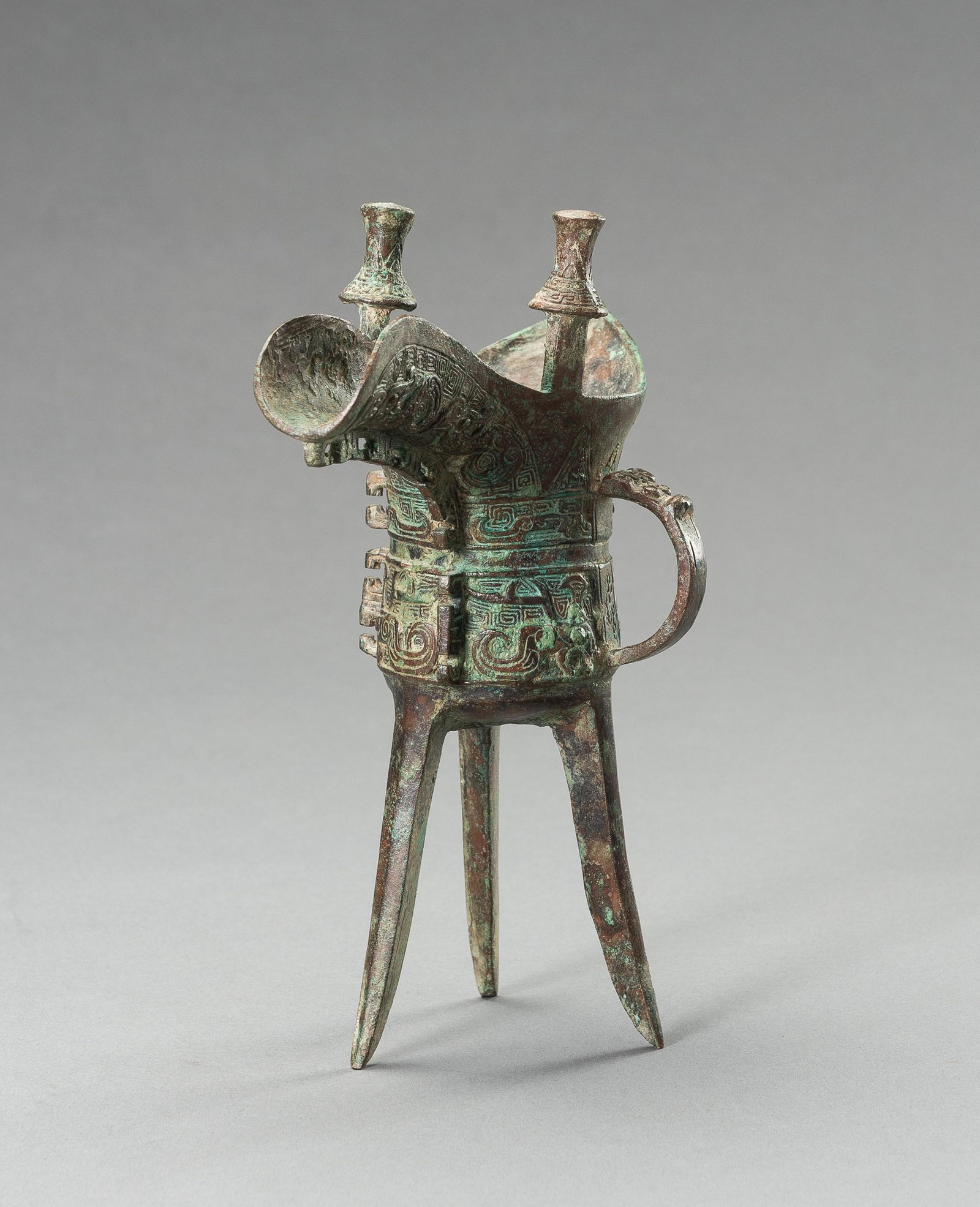 AN ARCHAISTIC SHANG-STYLE BRONZE RITUAL TRIPOD WINE VESSEL, JUE: AN ARCHAISTIC SHANG-STYLE BRONZE RITUAL TRIPOD WINE VESSEL, JUE China, late Qing Dynasty (1644-1912) to Republic period (1912-1949). The tripod vessel raised on three tall blade-shaped feet and cast w