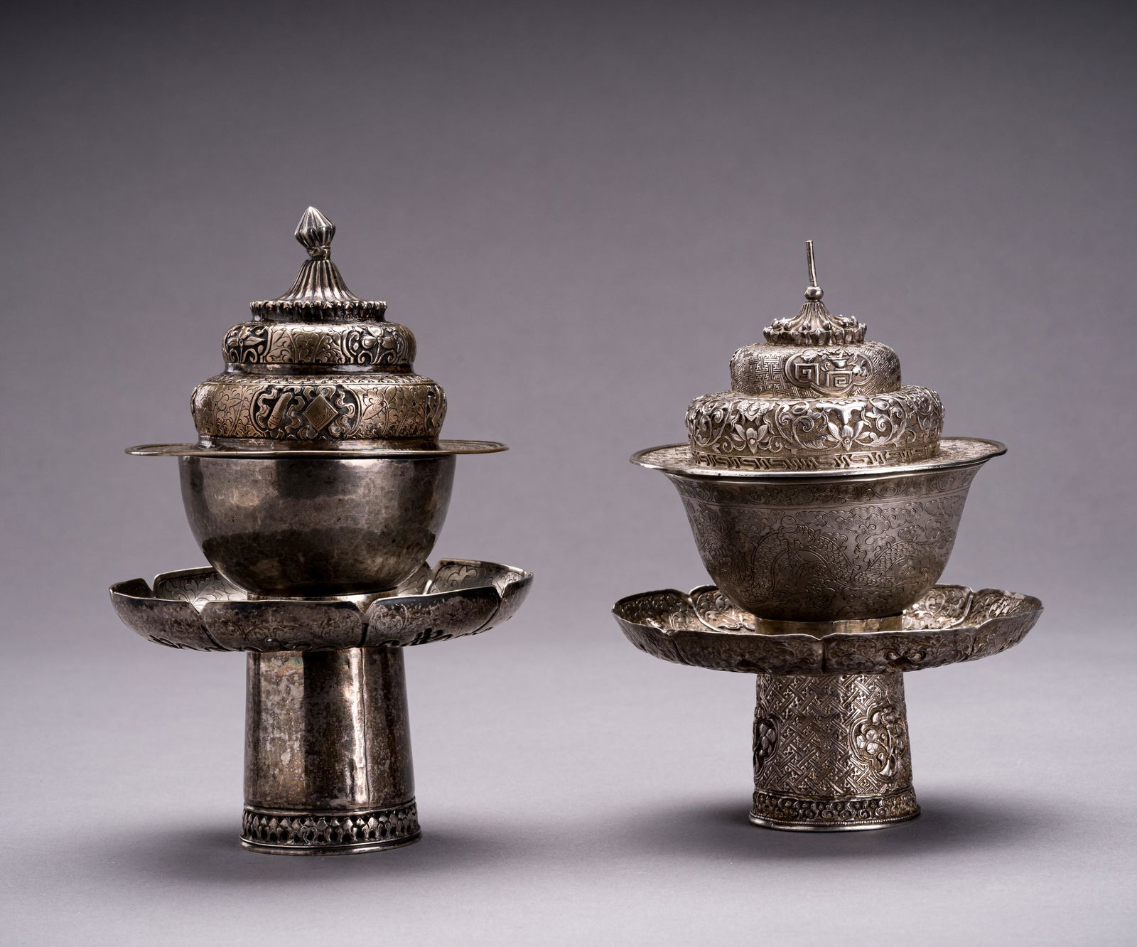 TWO SILVER BUTTER TEA SETS, QING DYNASTY: TWO SILVER BUTTER TEA SETS, QING DYNASTY Tibetan-Chinese, 19th century. Comprising a silver cup, stand, and cover. The silver elements are finely embossed and engraved with floral decor, dragons, and